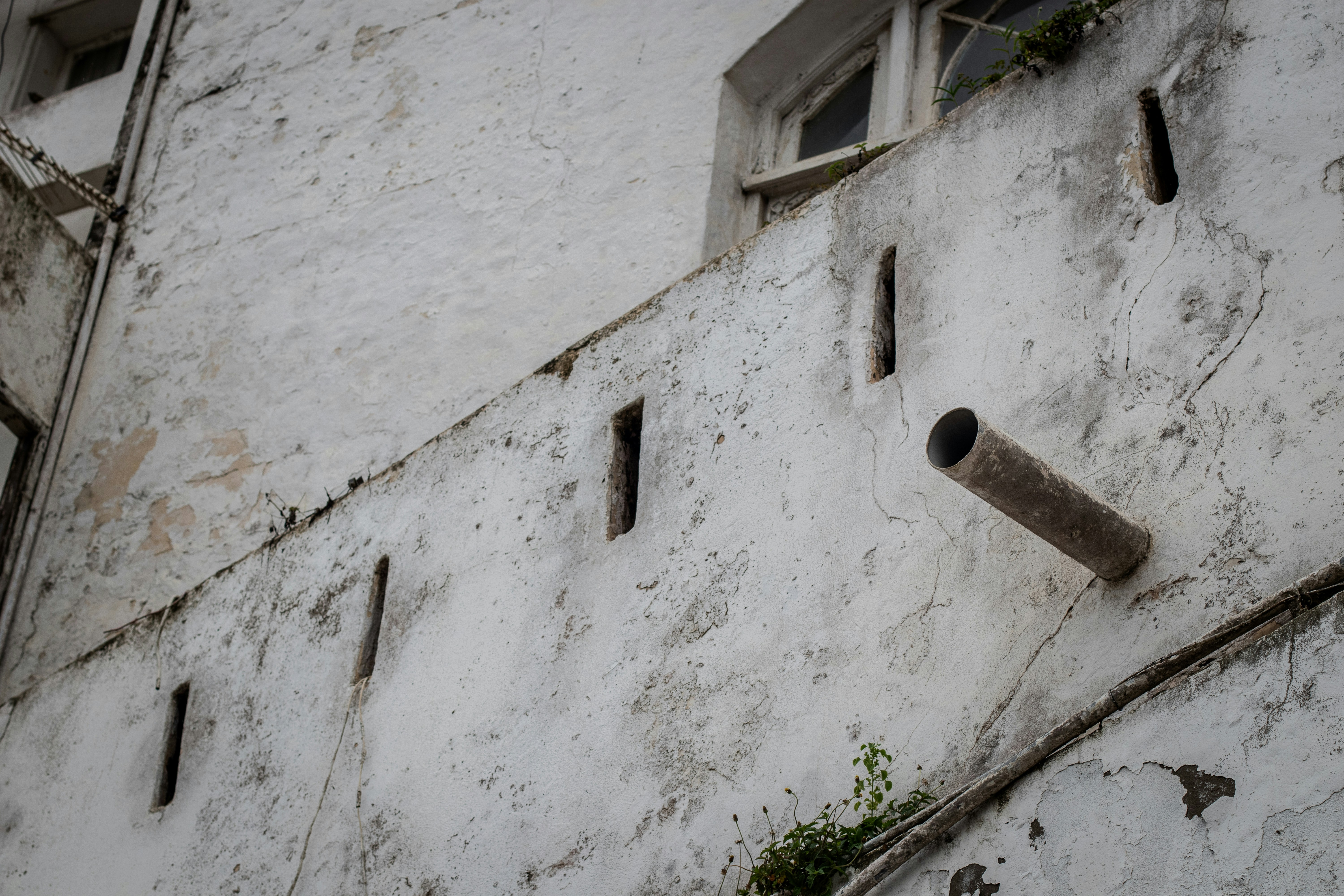 Muro bianco consumato dal tempo con tubo, finestra e strette aperture di ventilazione