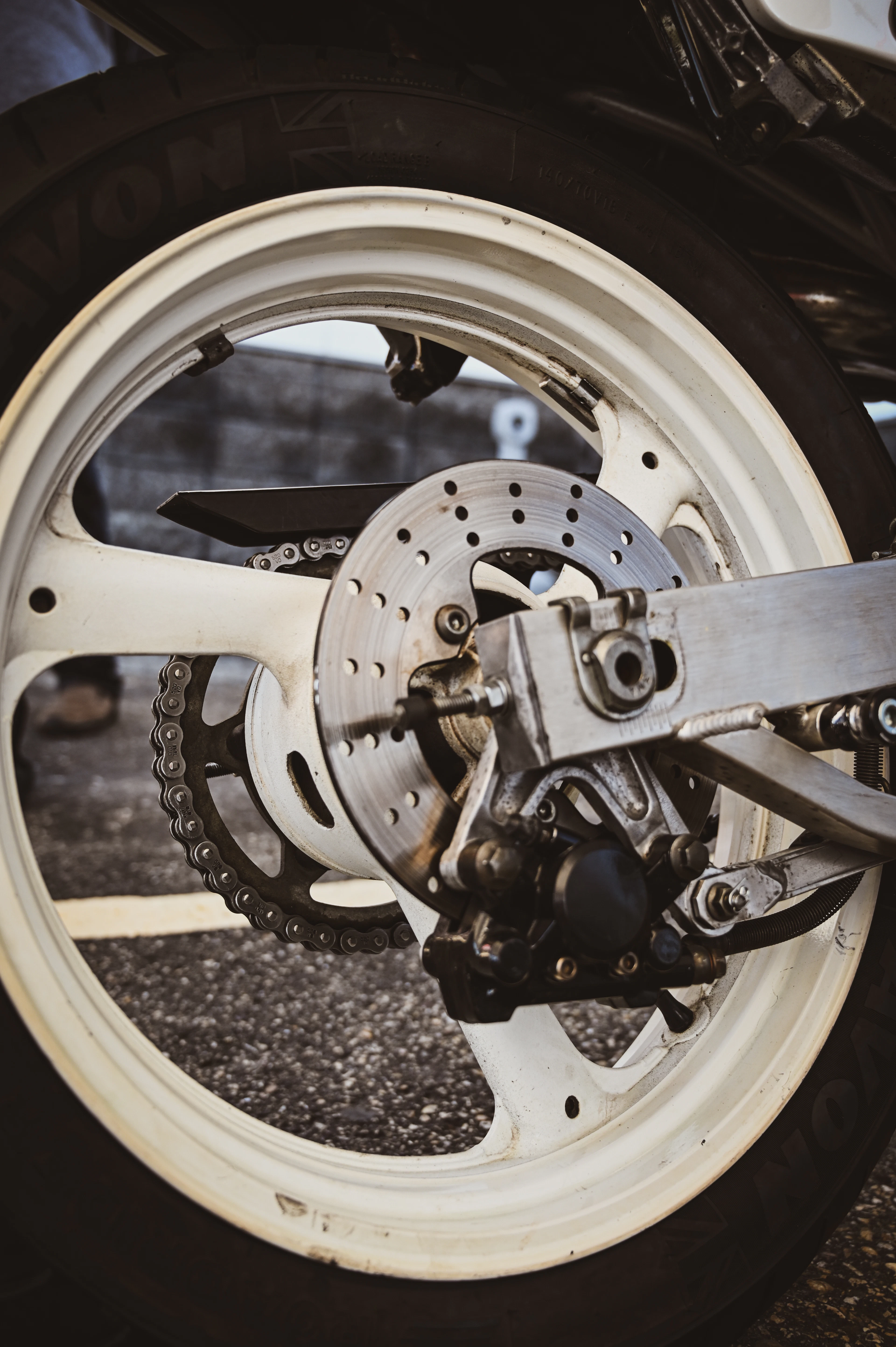 A drilled brake disc and caliper on a white rear wheel