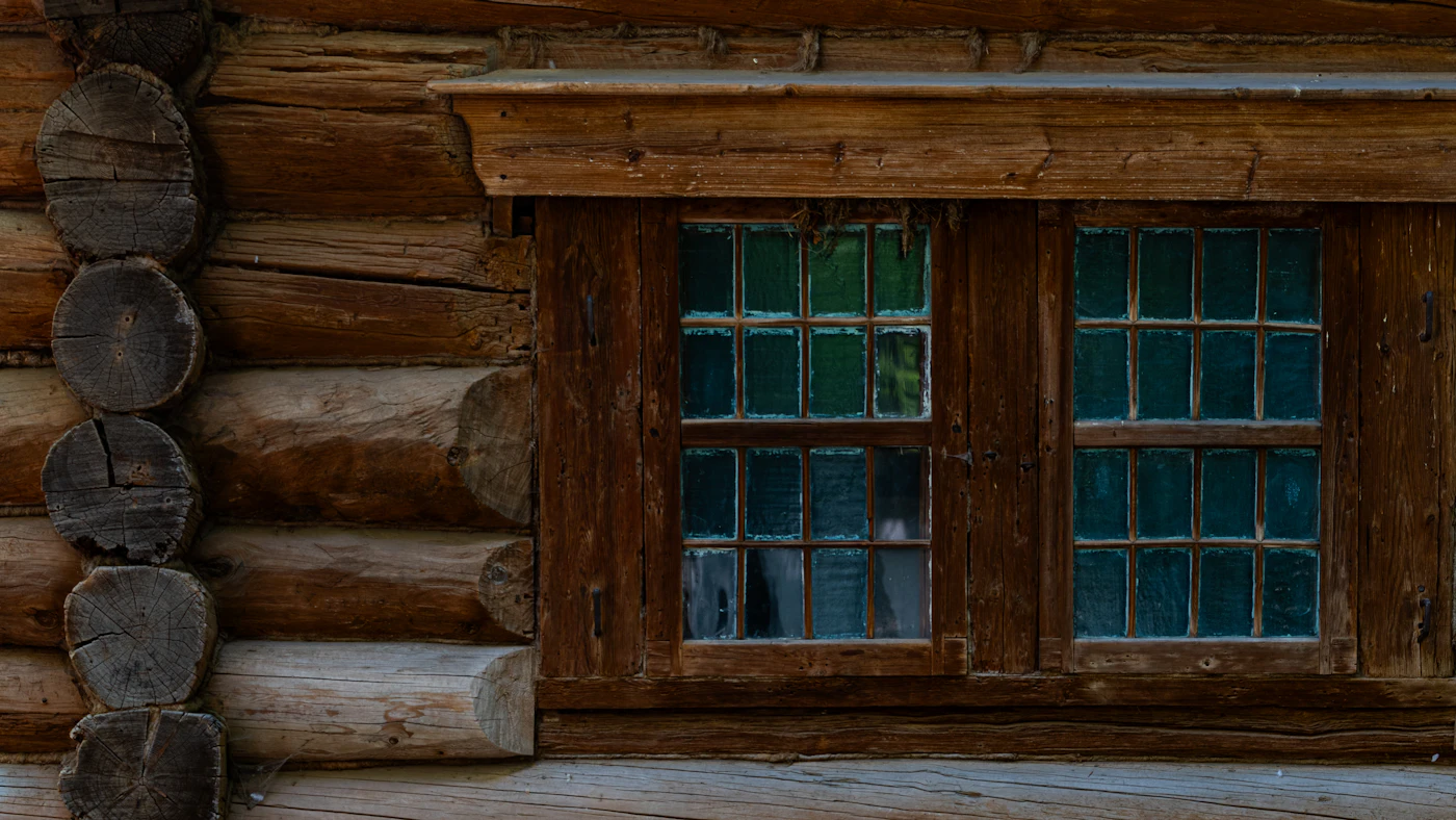 Close-up of a rustic log cabin wall with two framed windows