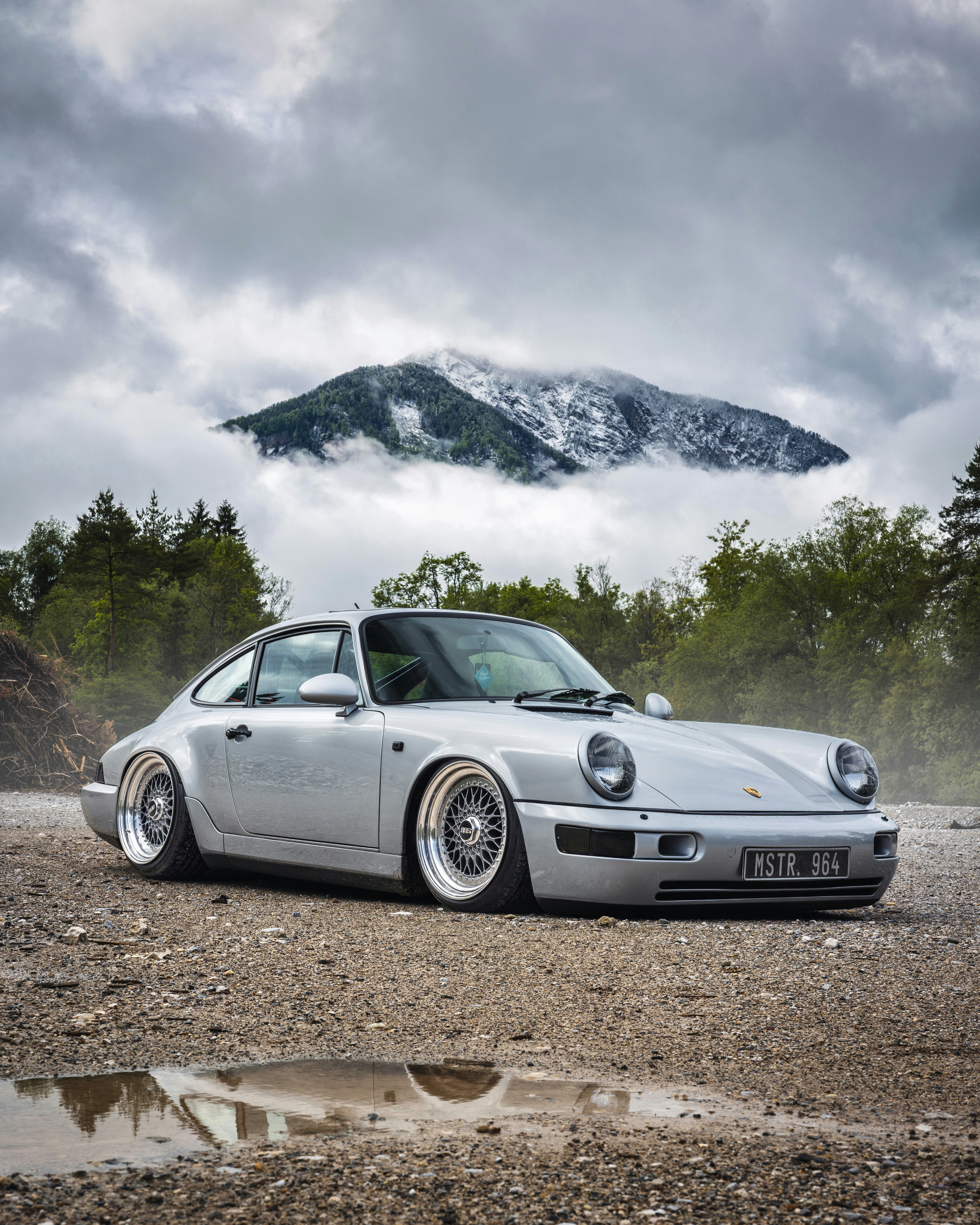 Coche Porsche plateado sobre grava con fondo de montaña nevado