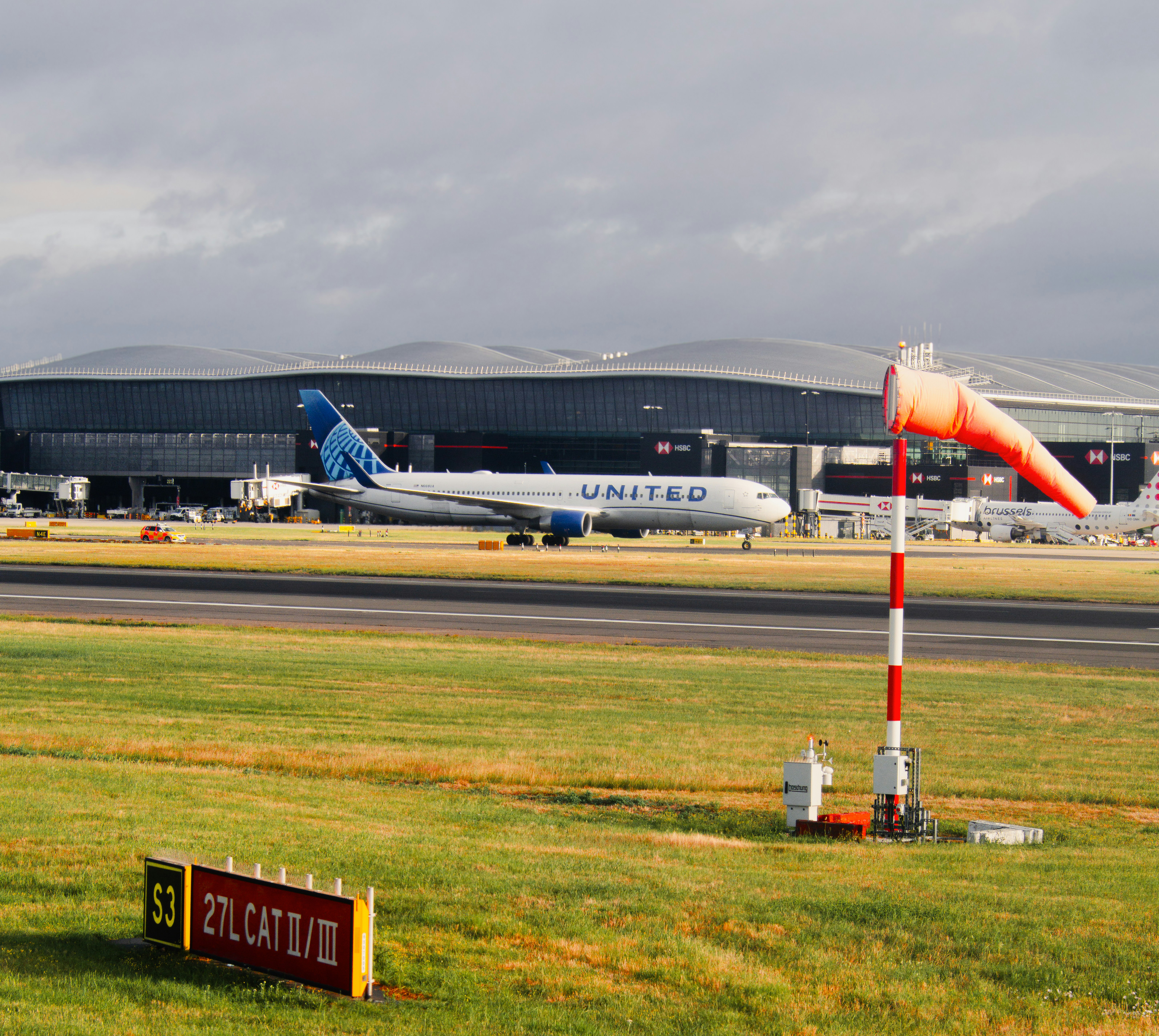 United airplane on airport runway with windsock and terminal.
