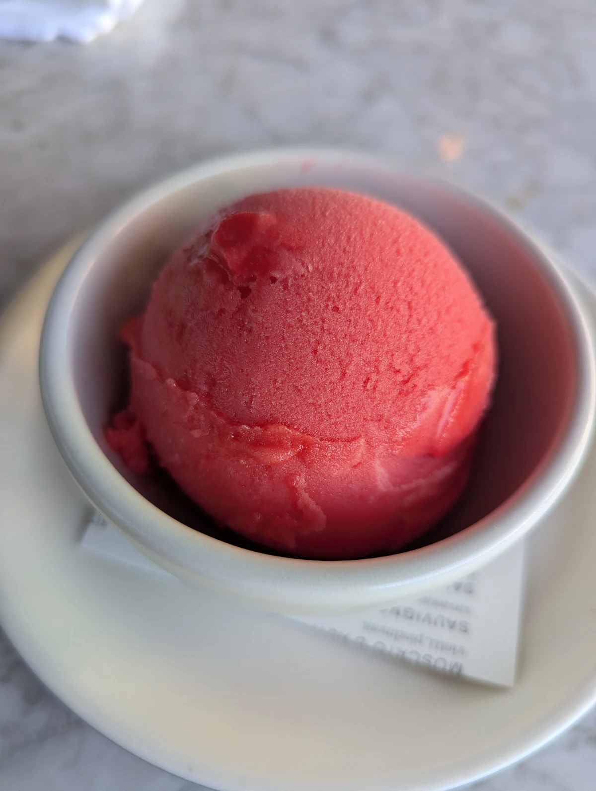 A single scoop of bright pink sorbet in a white bowl, shot close