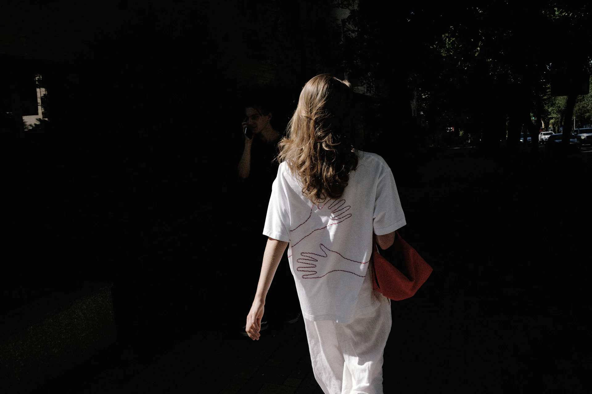 Woman in white walking away with a red bag.