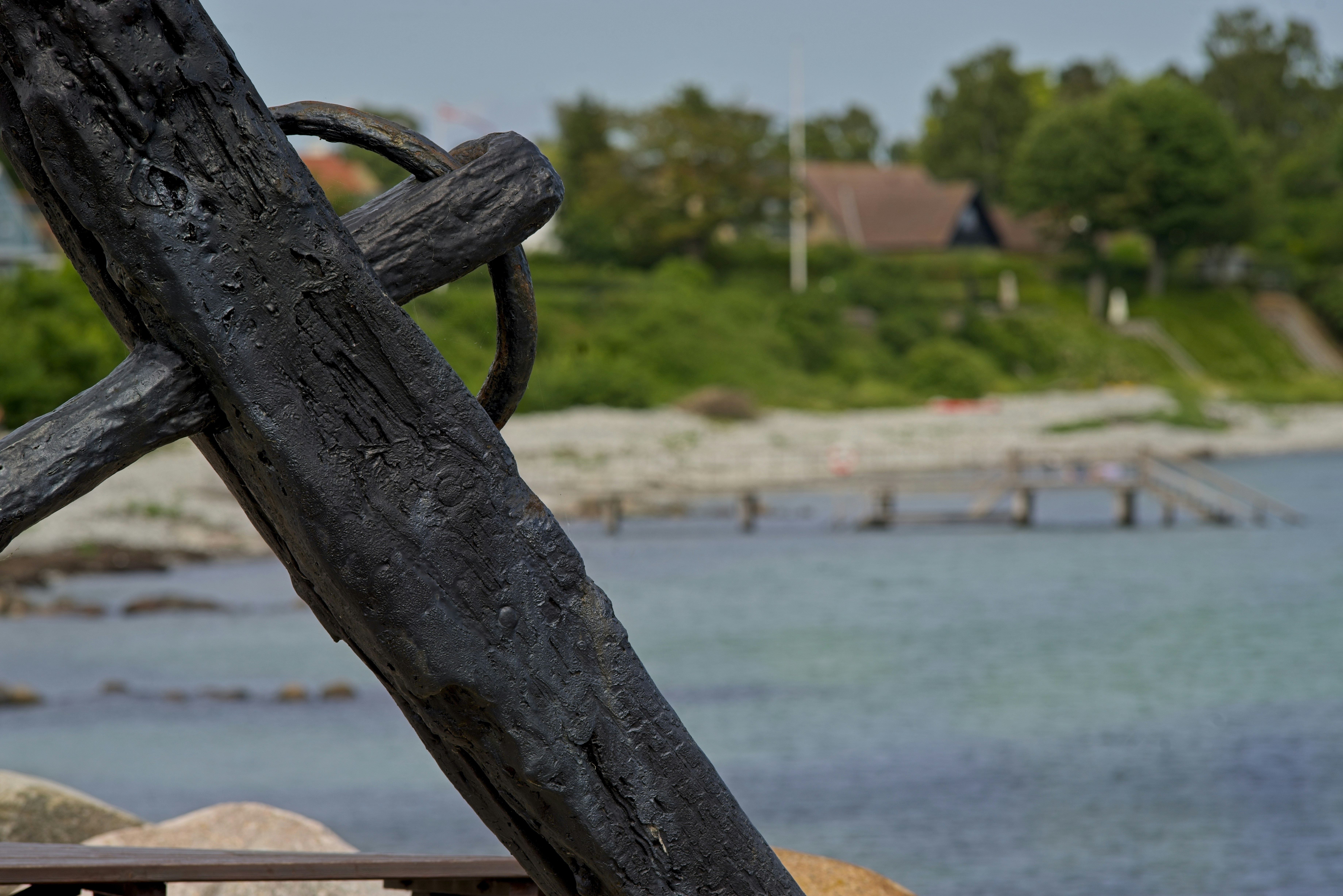 Dunkler Holzbalken, der auf ruhiges Wasser, einen entfernten Pier und ein Haus blickt.
