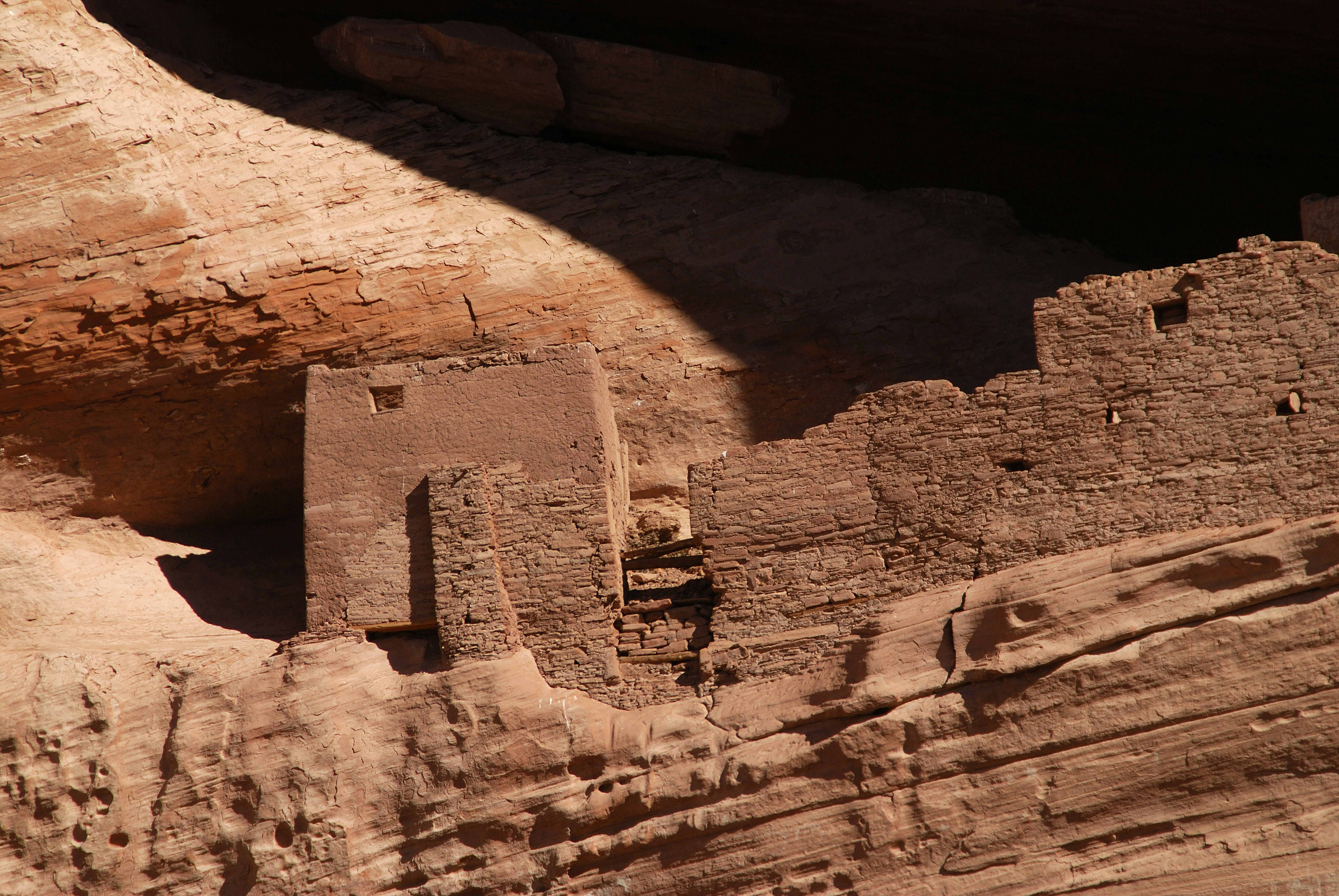 Ancient cliff dwellings built into a reddish rock face - archaeological sites