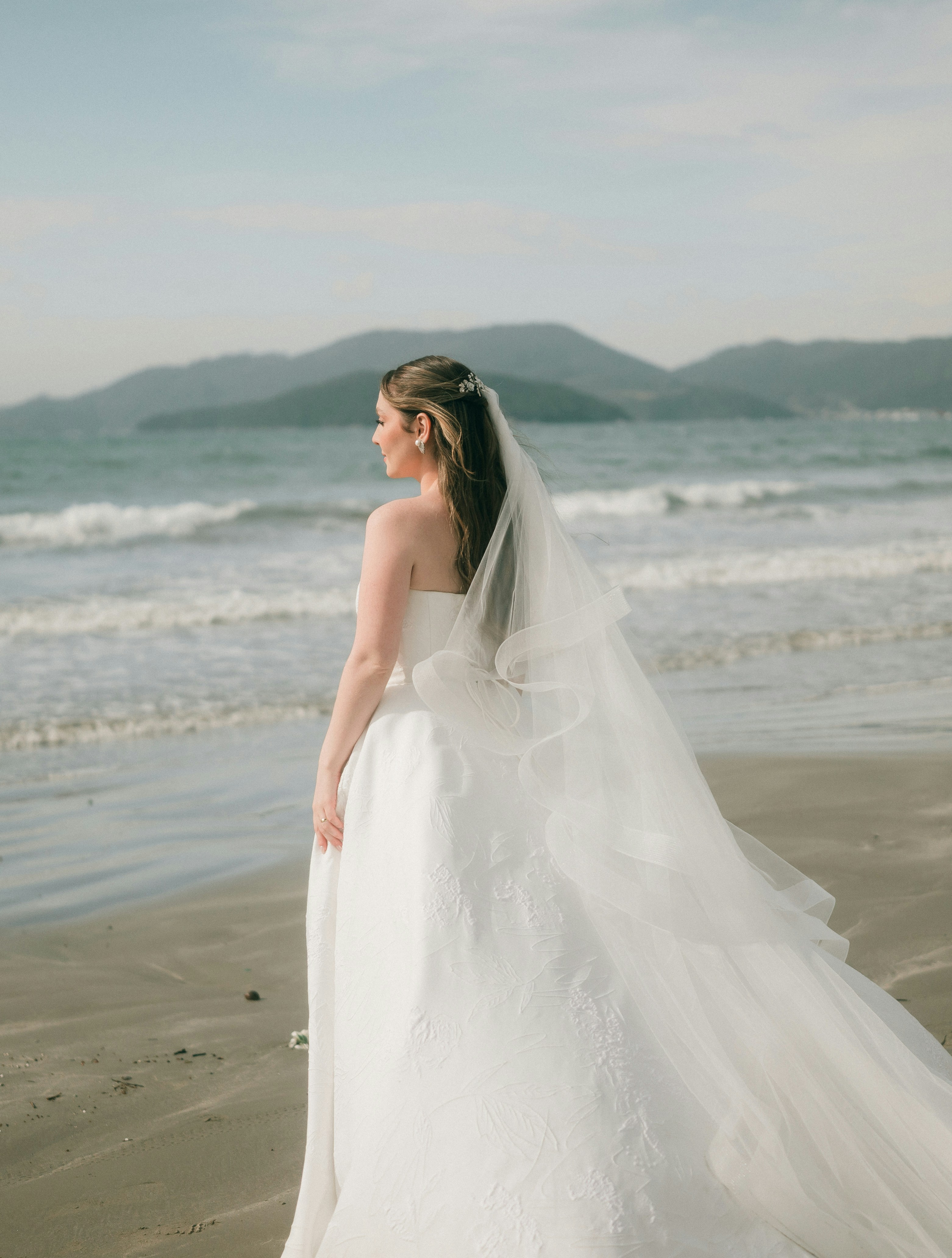 Una novia está de pie en una playa de arena junto al mar.