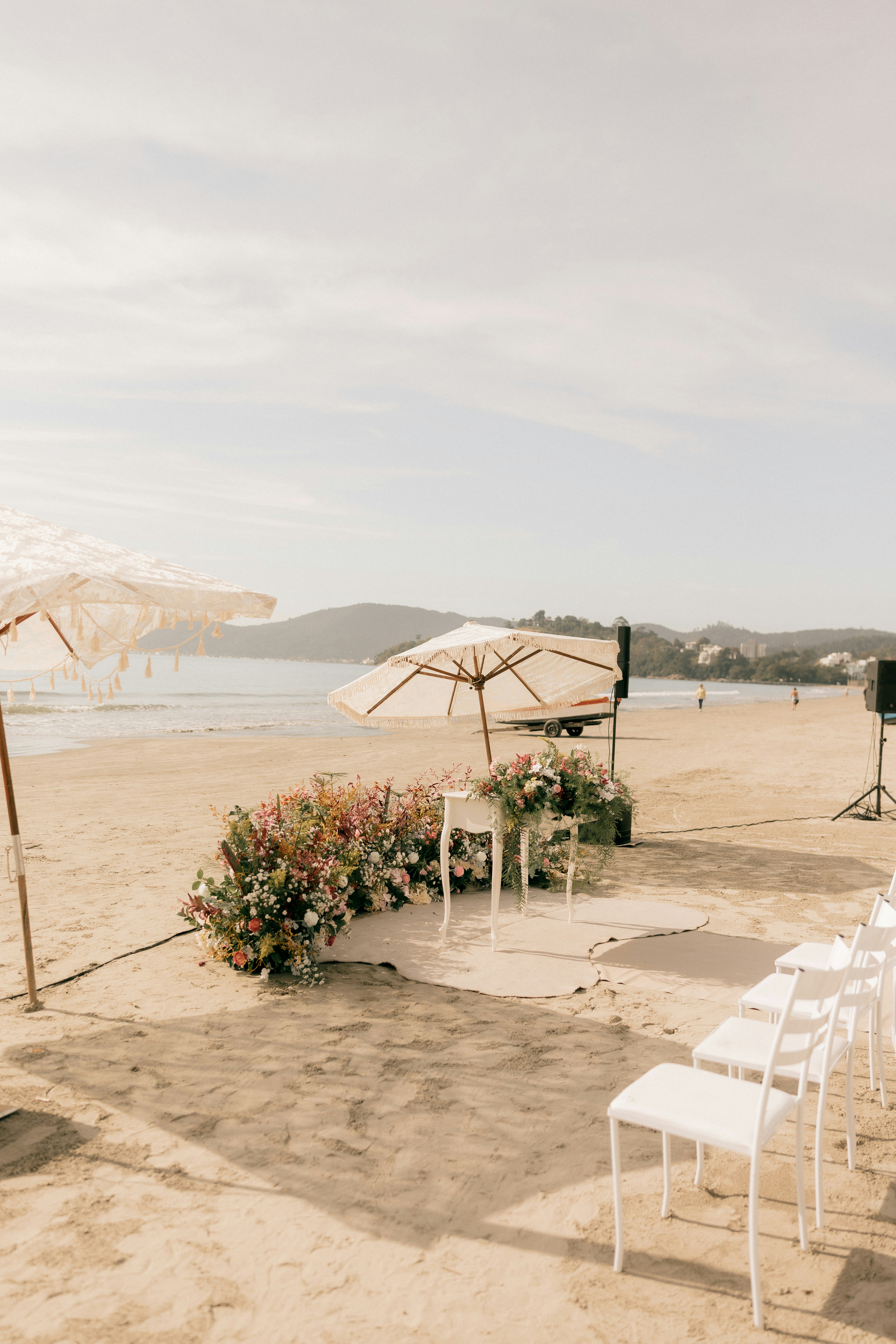 Montaje de boda en la playa con sillas blancas, sombrillas y flores de colores.