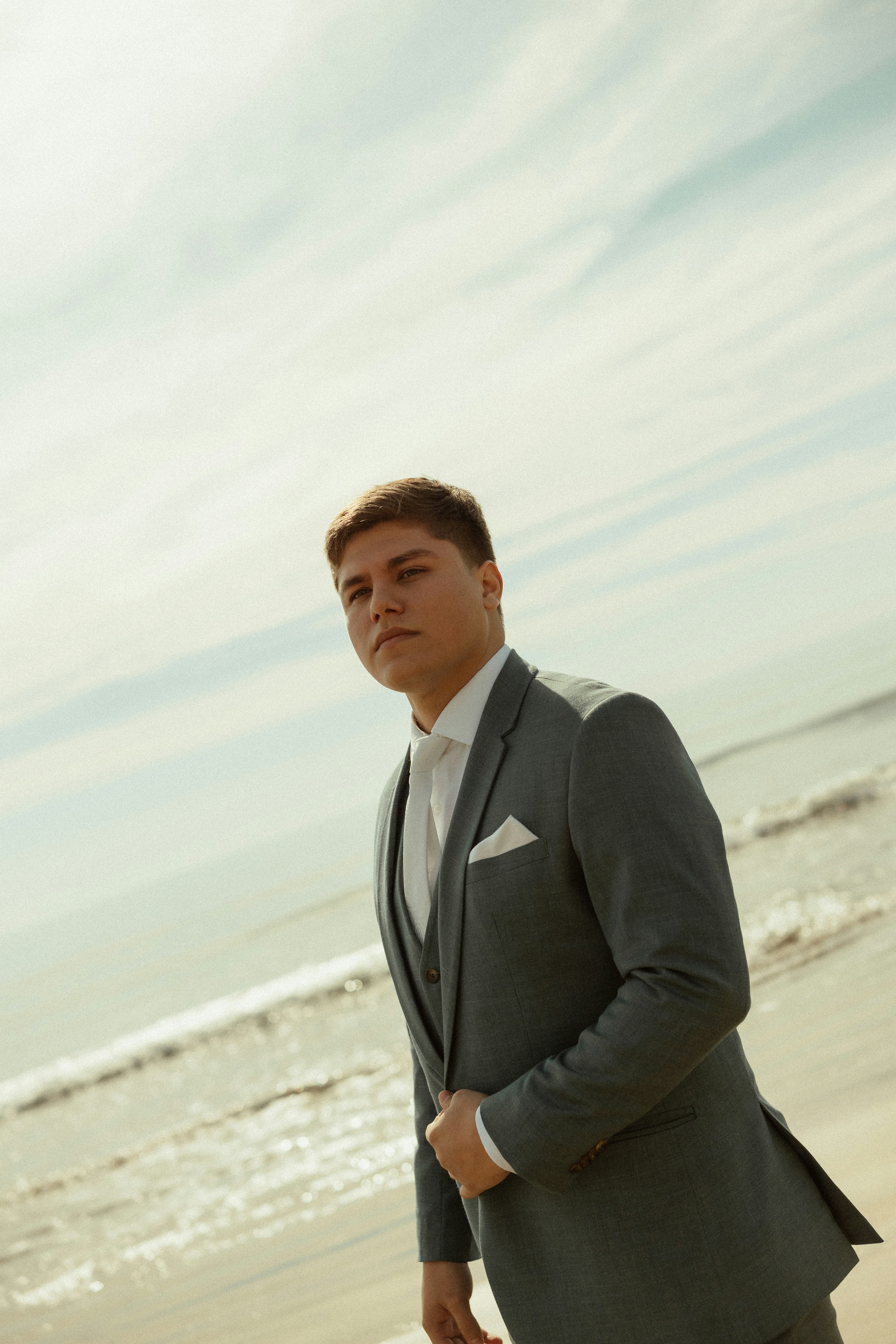 Joven con traje gris de pie en una playa.