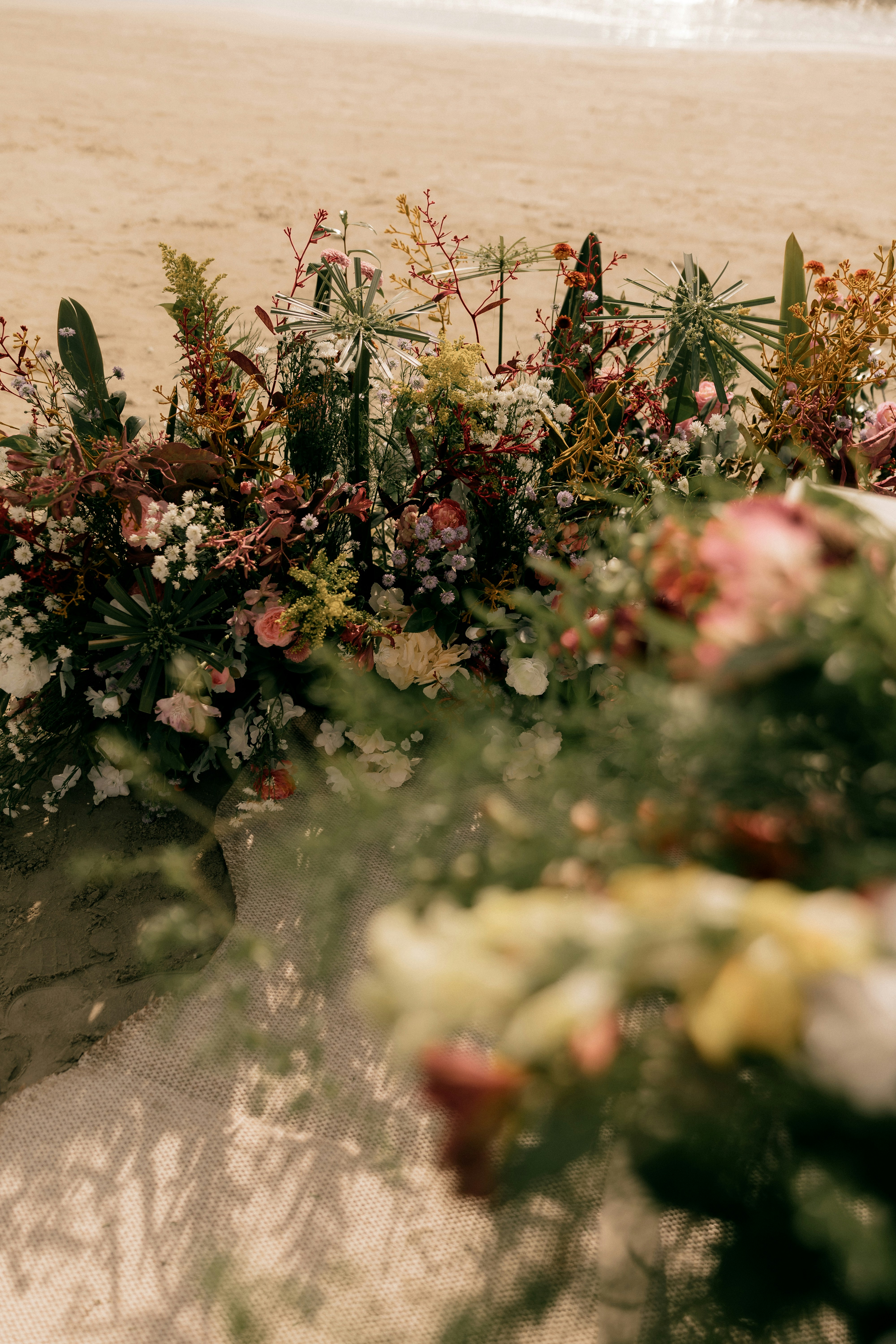 Arreglos florales en una playa de arena con el océano de fondo.