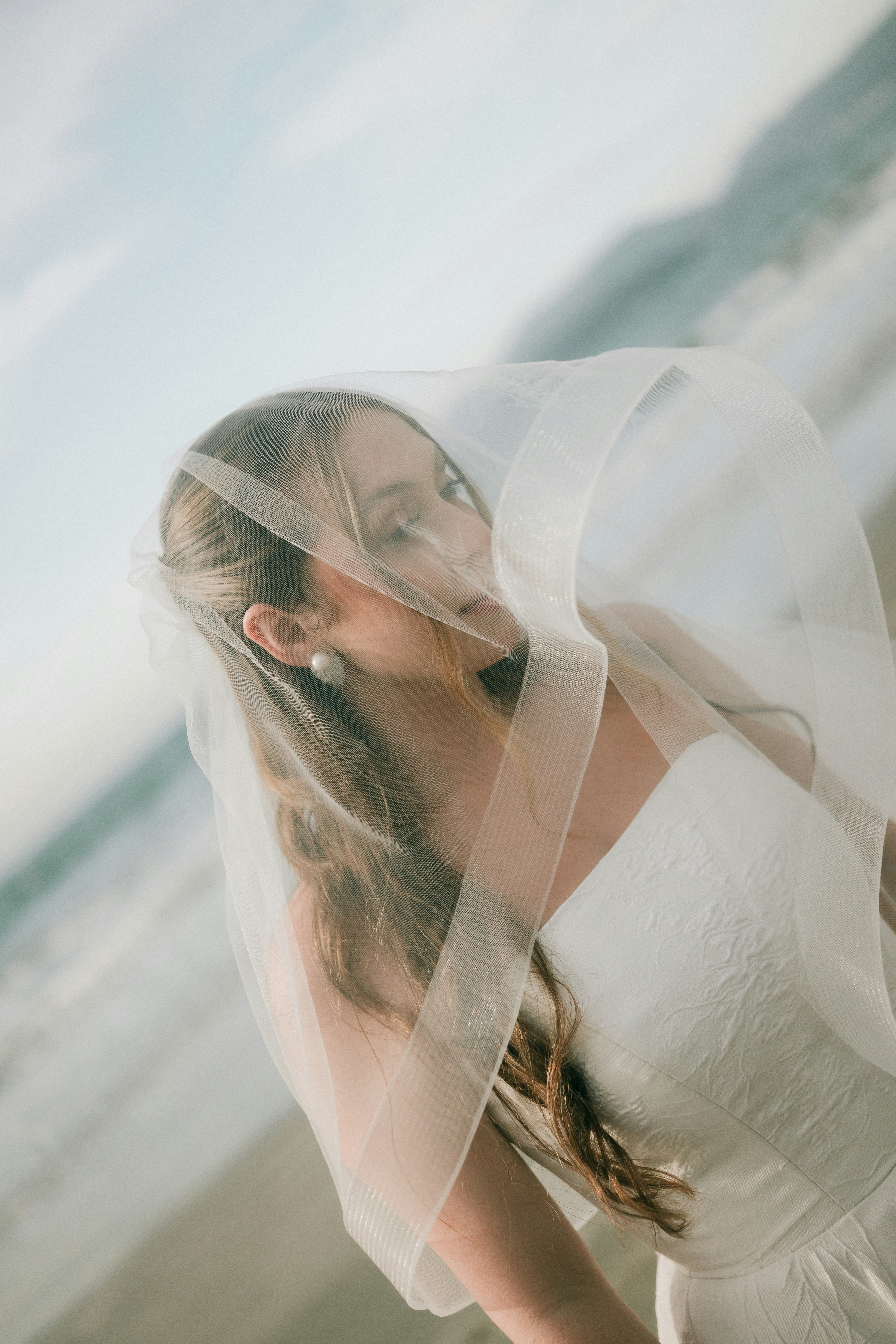 Mujer con vestido de novia y velo junto al mar.