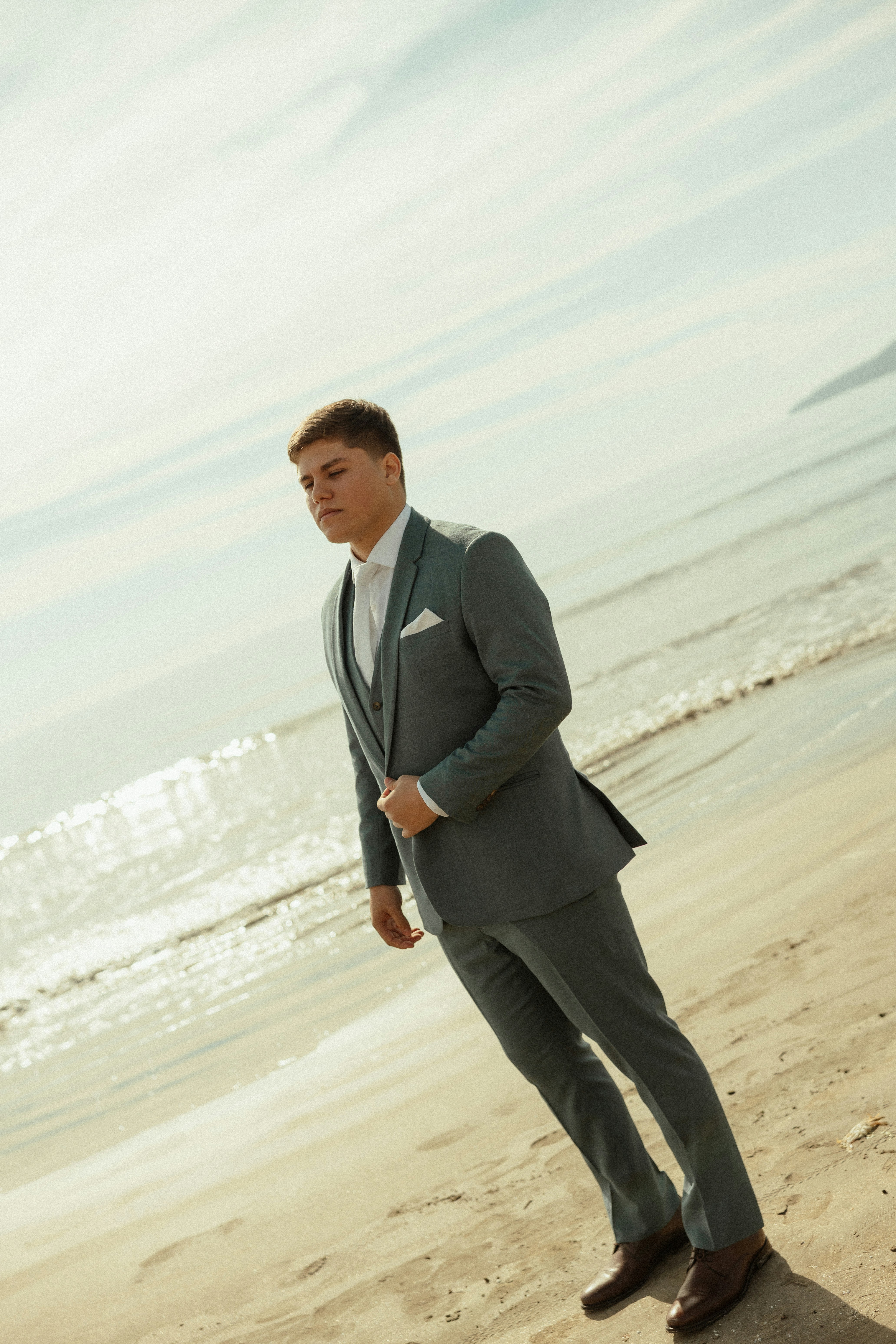 Joven con traje gris de pie en una playa.