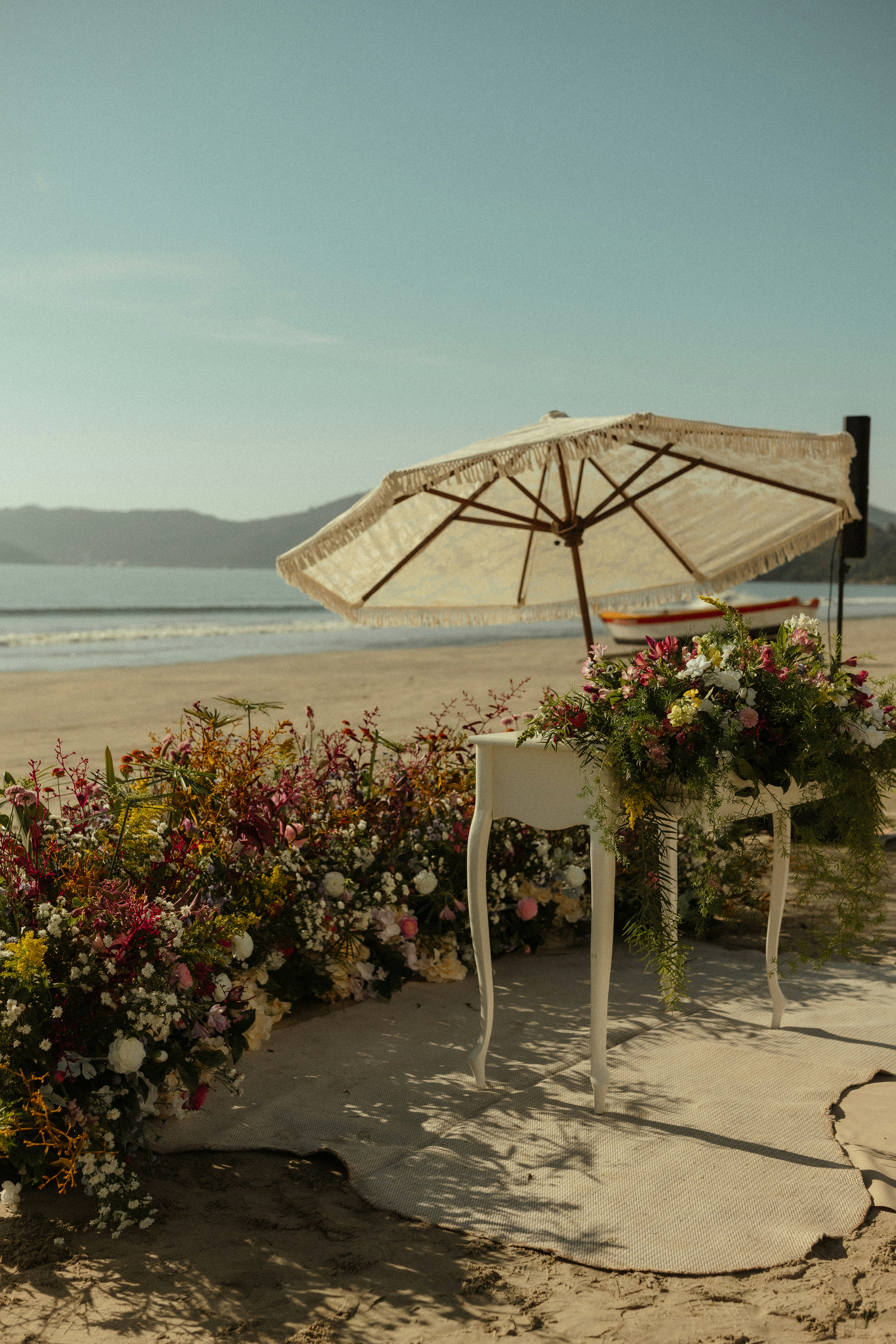 Una boda en la playa con sombrilla, mesa y flores.