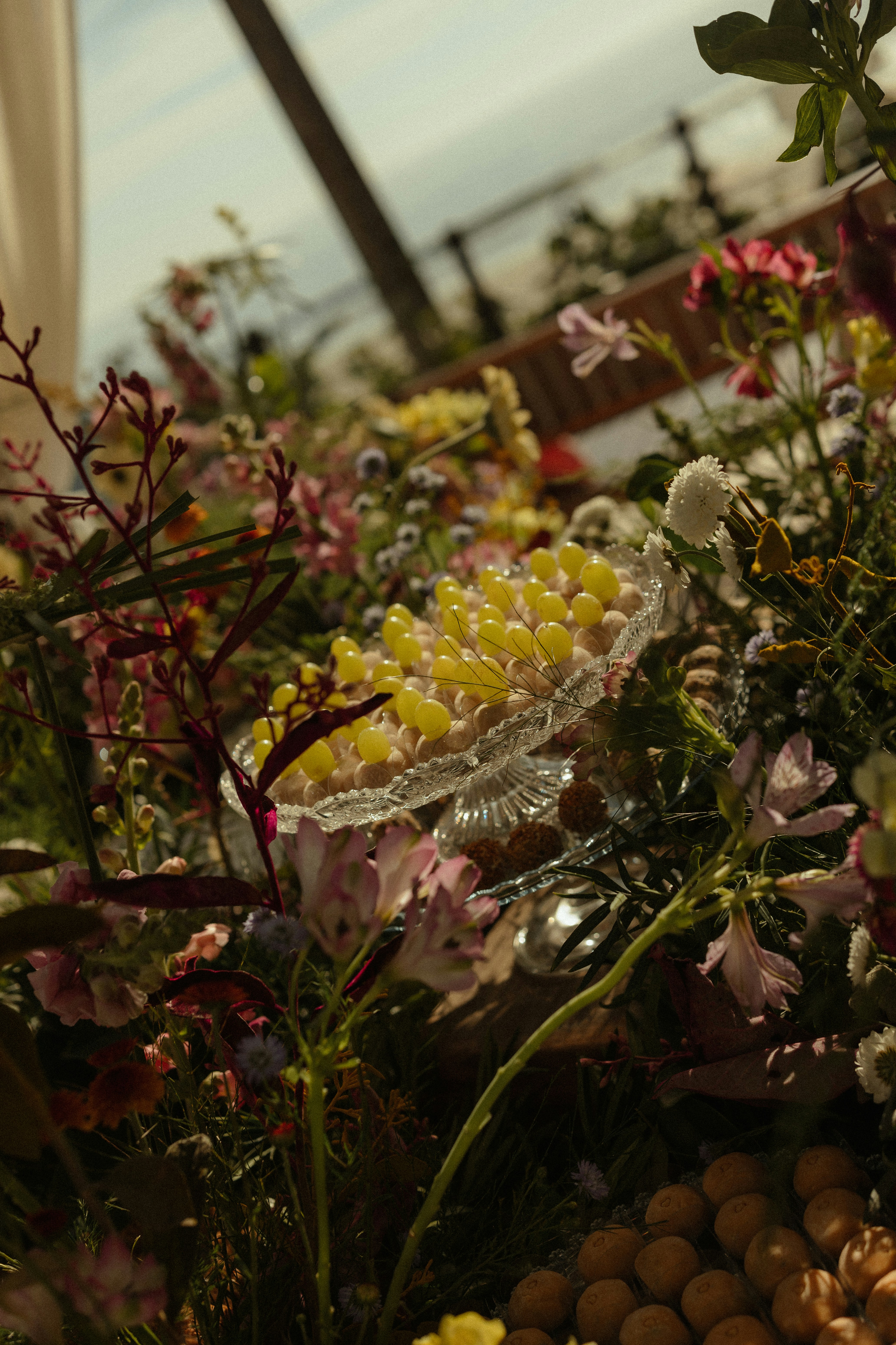 Un recipiente de cristal con caramelos amarillos rodeado de flores coloridas.
