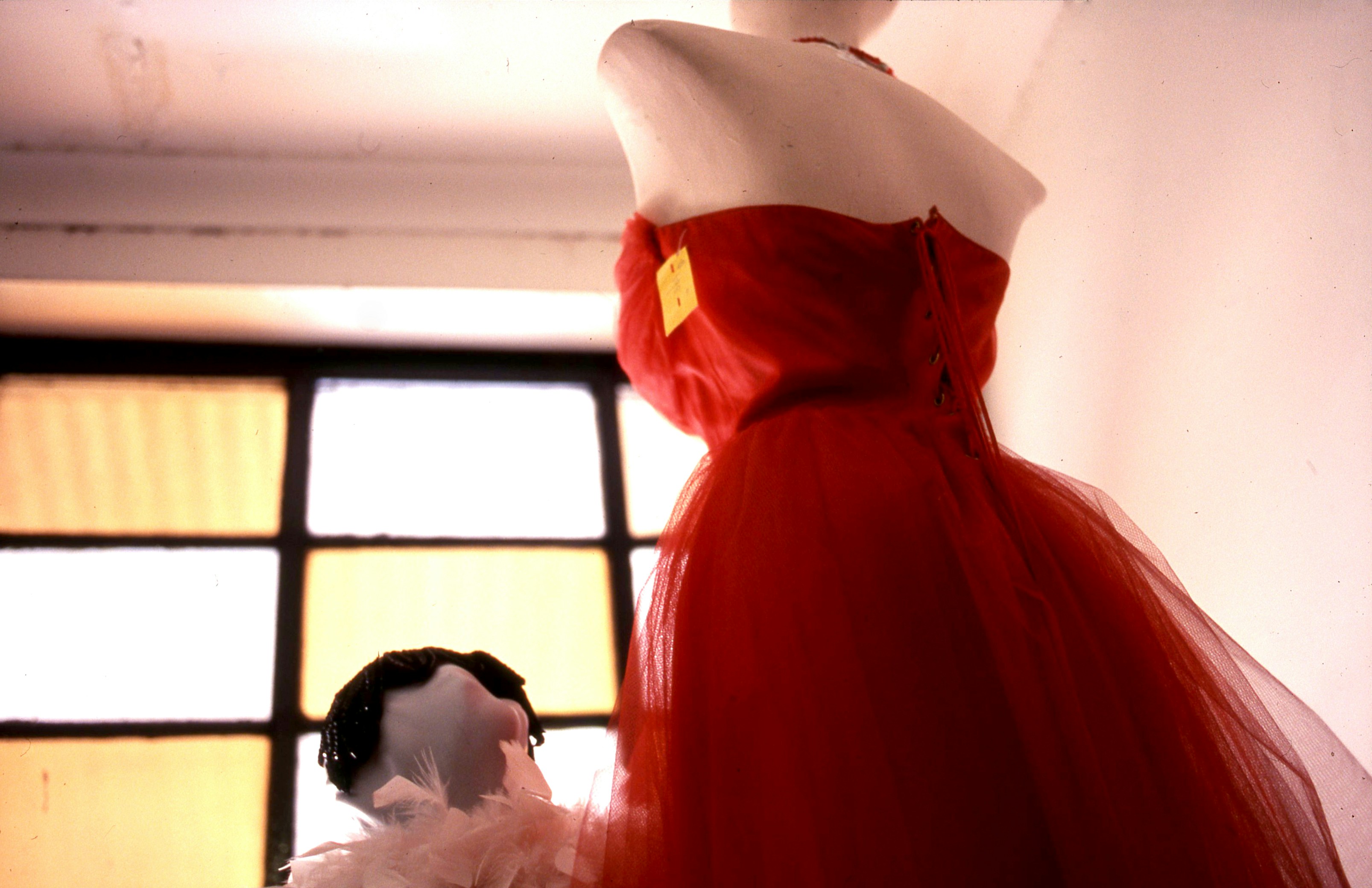 Un maniquí exhibe un vestido rojo vibrante cerca de una ventana.