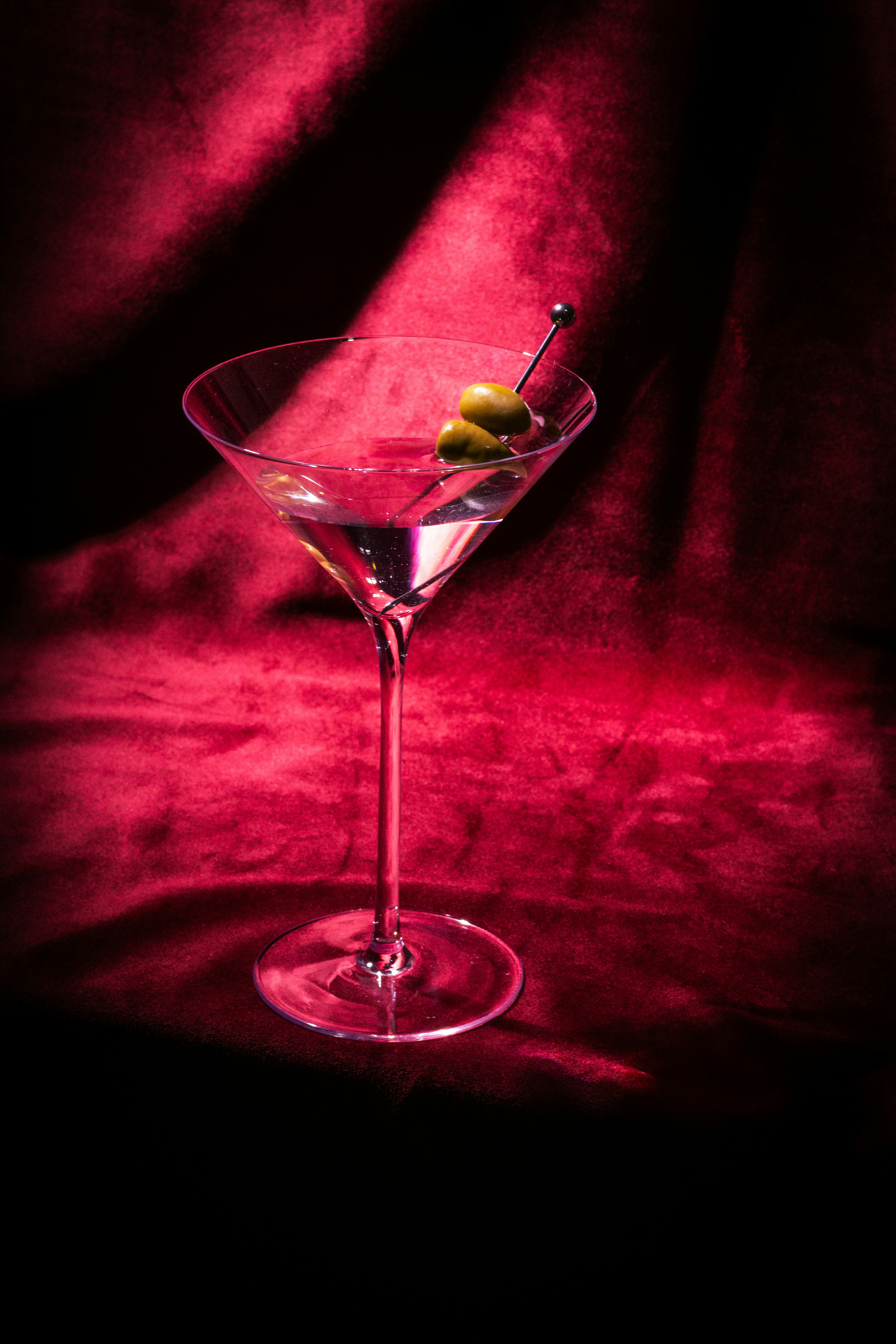 Martini glass with olives against a dramatic red backdrop
