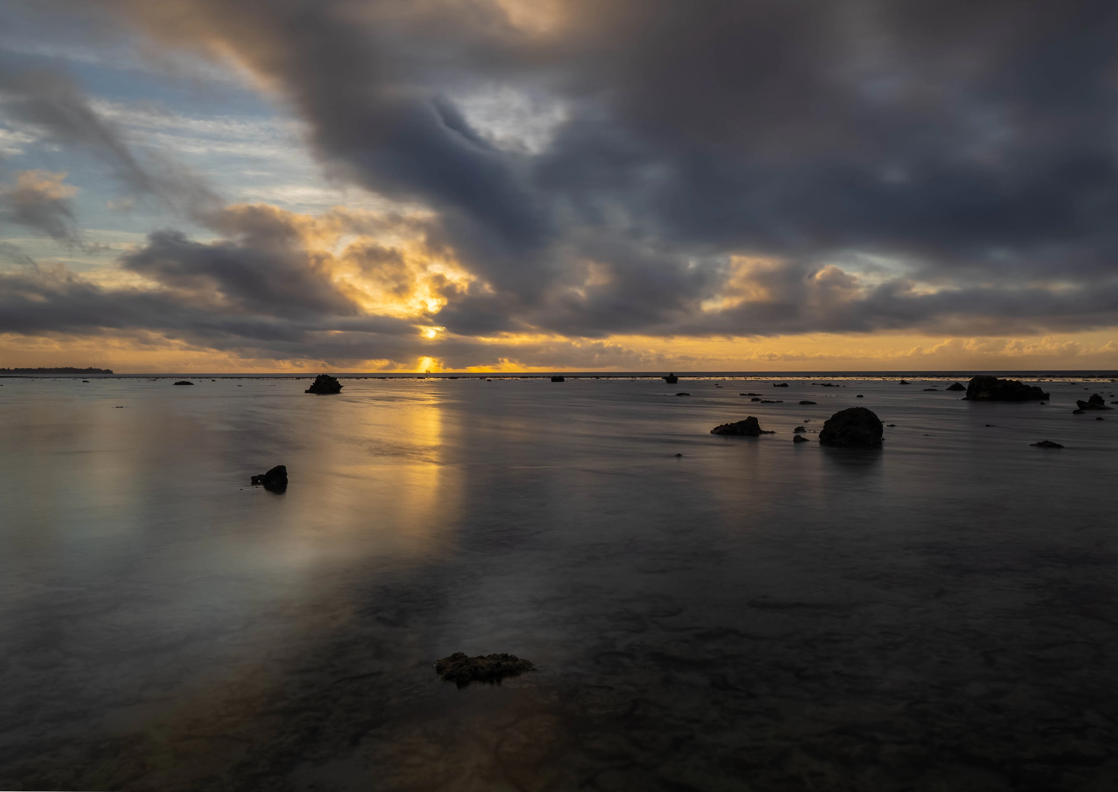 Sunset over calm, shallow water scattered with rocks by the beach at Tamarind House, Avarua, on Rarotonga