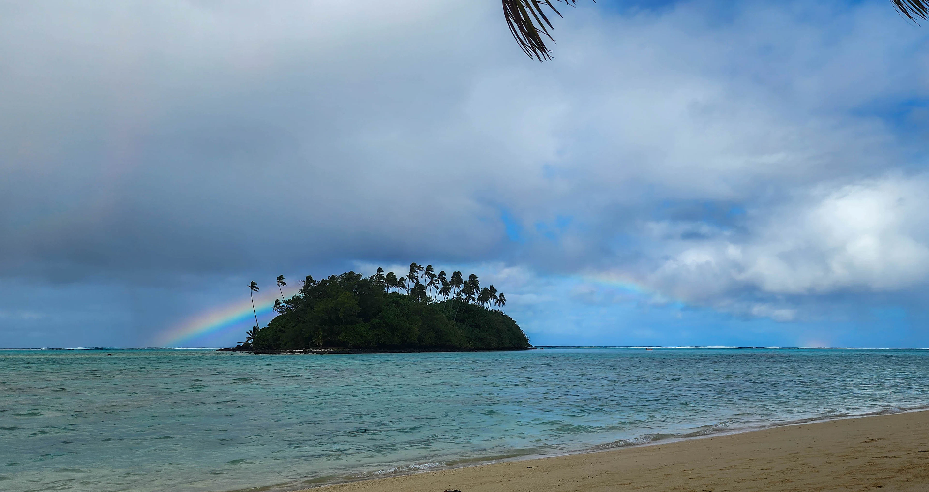 A rainbow over the palm-covered motu of Taakoka, seen from Muri Beach, Rarotonga