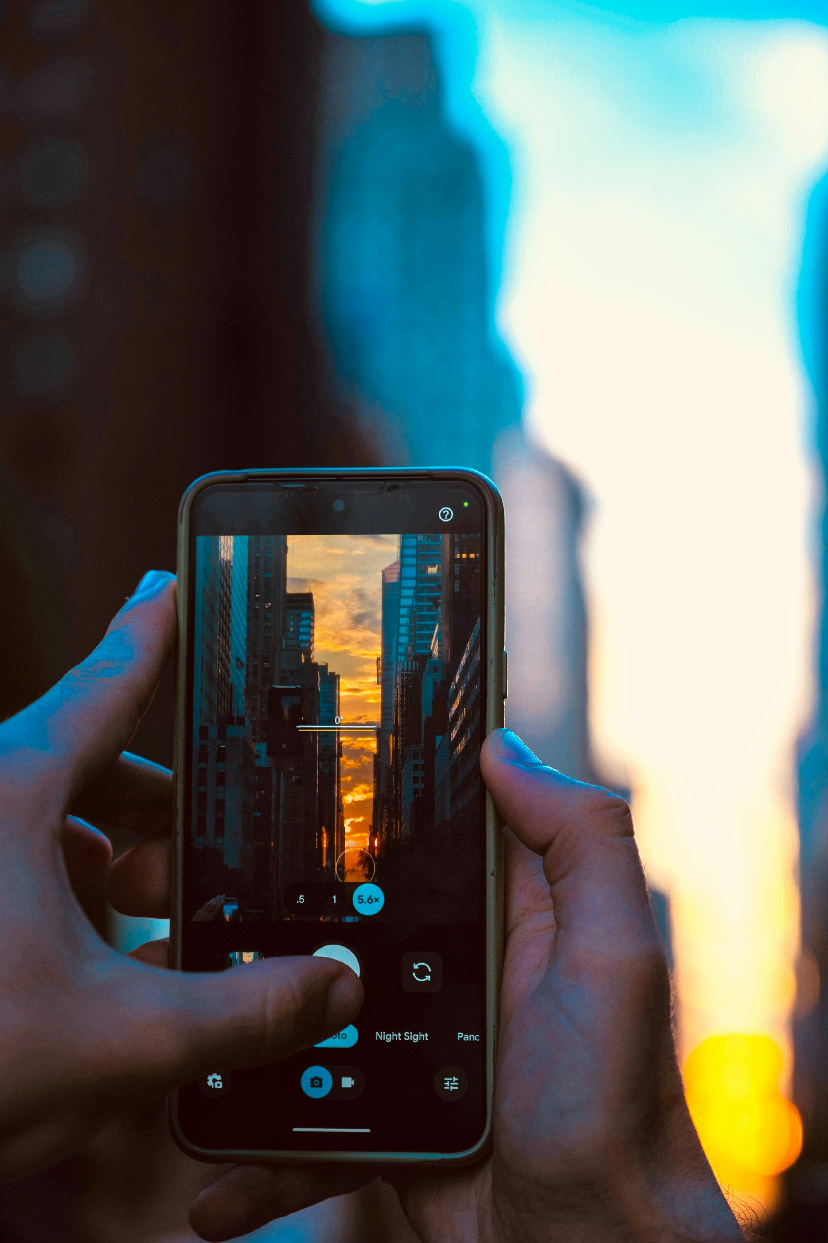 Hands holding a smartphone capturing a city sunset