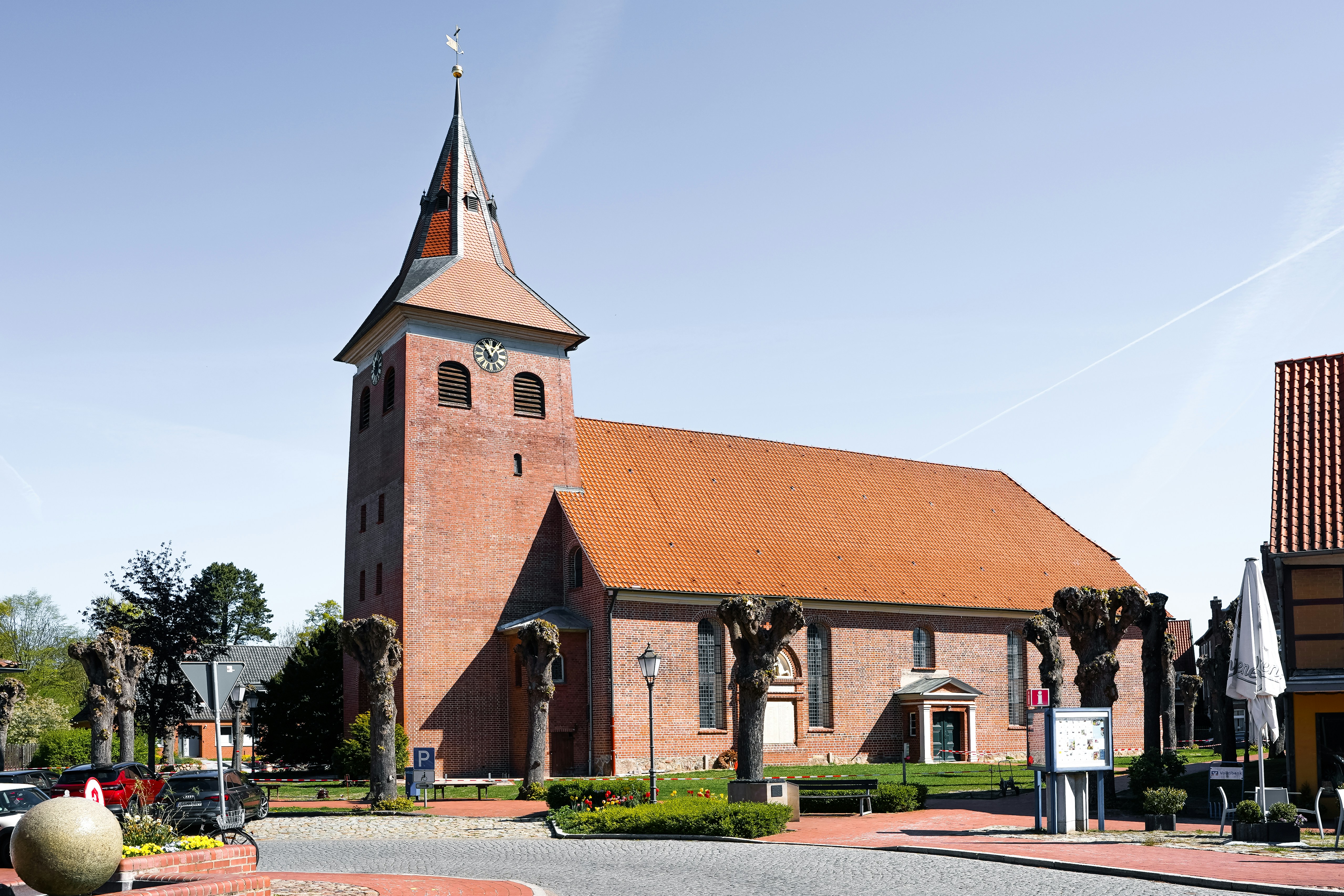 Red brick church with a tall steeple under blue sky.