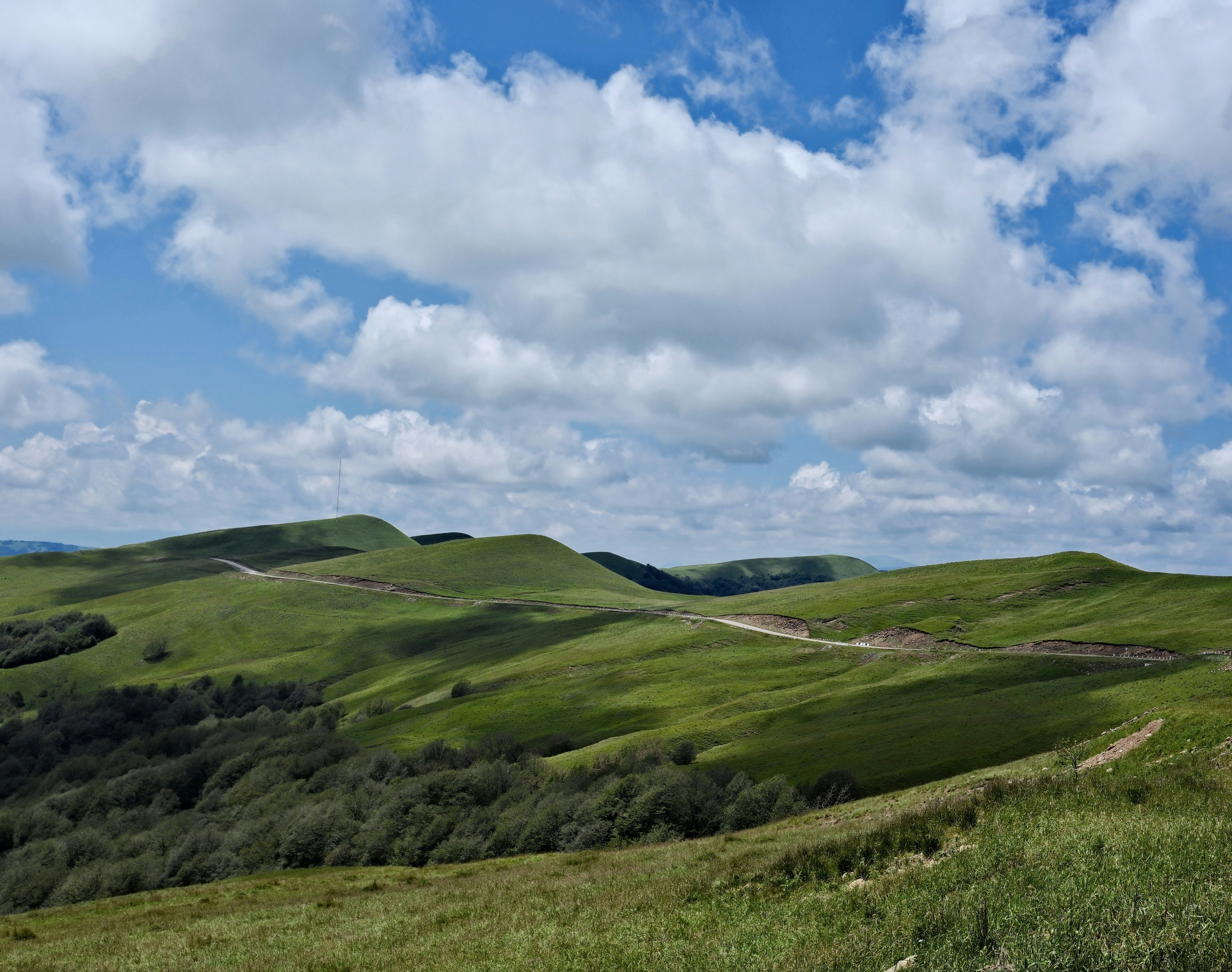Green hills and winding road under a cloudy blue sky