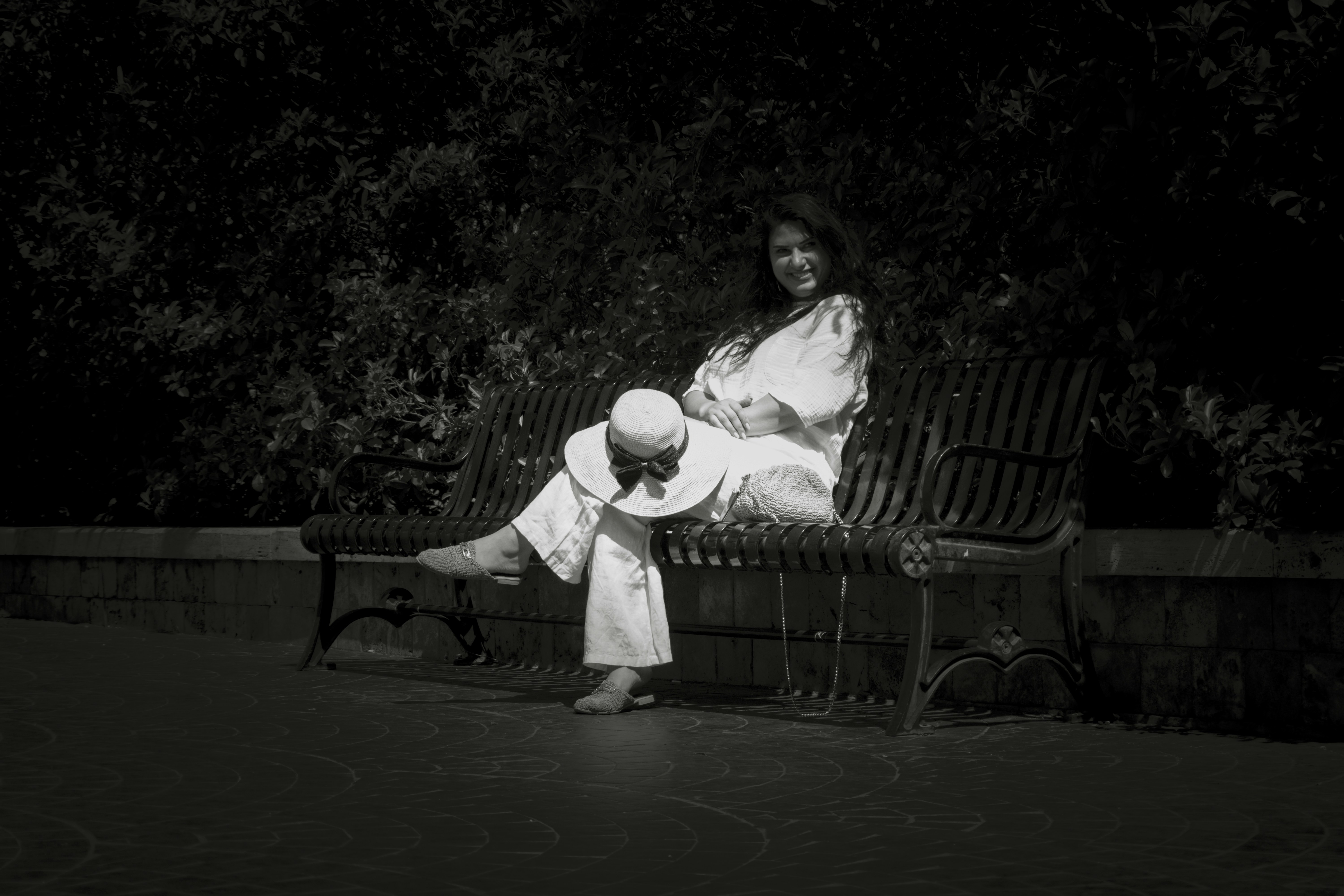 A woman sits on a bench, holding a hat