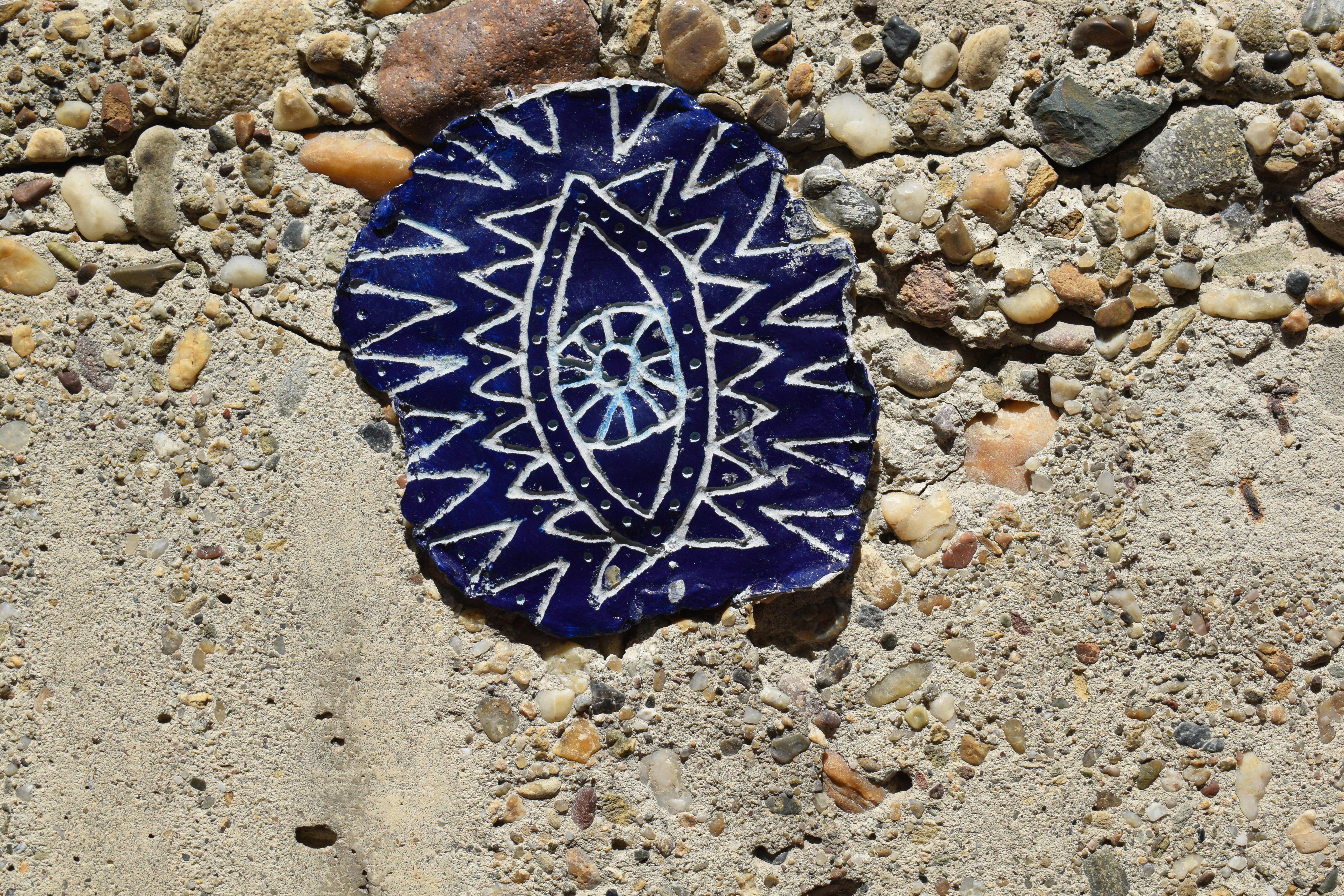 Blue ceramic shard with an abstract eye on concrete.