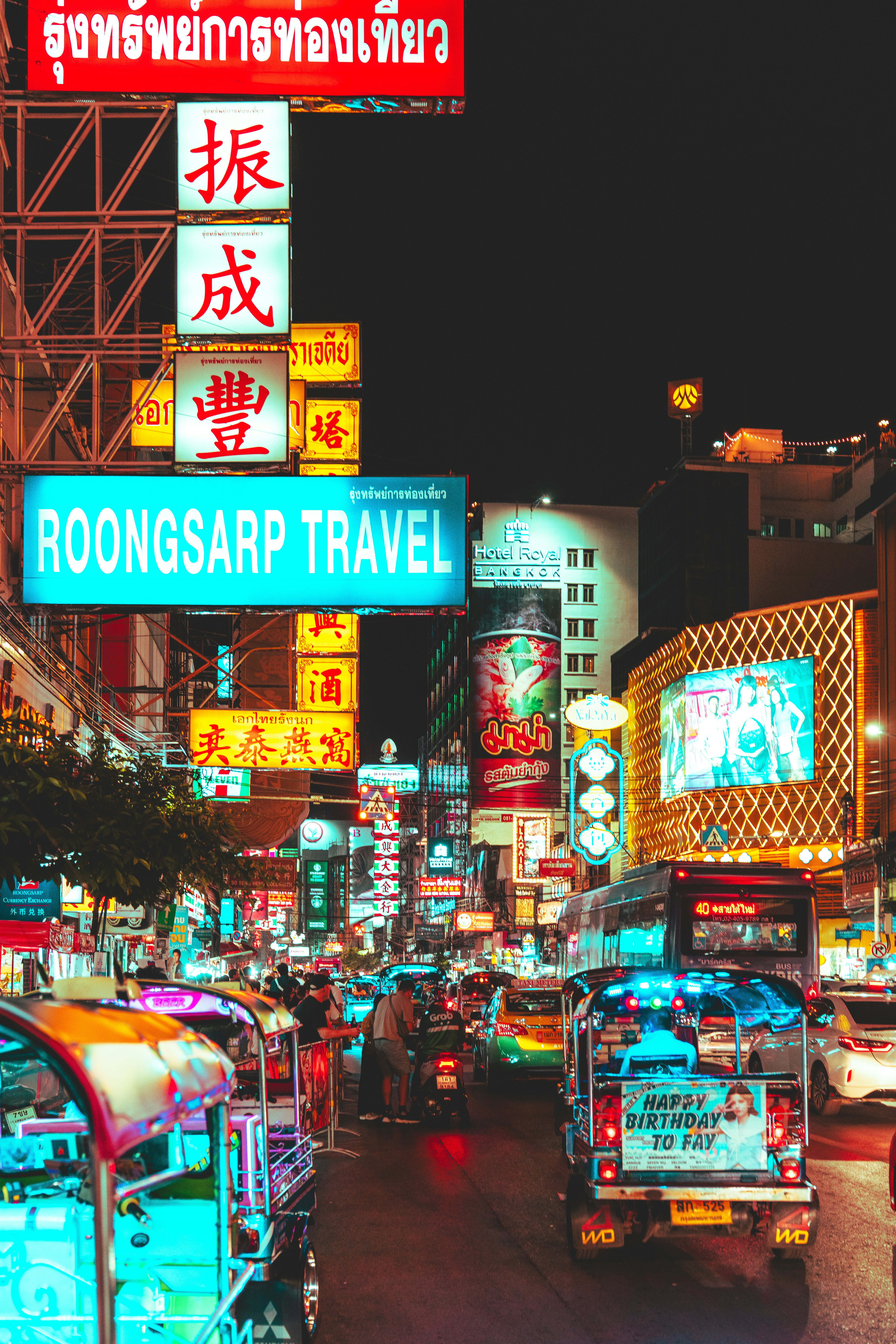 Busy street at night with neon signs and tuk-tuks.