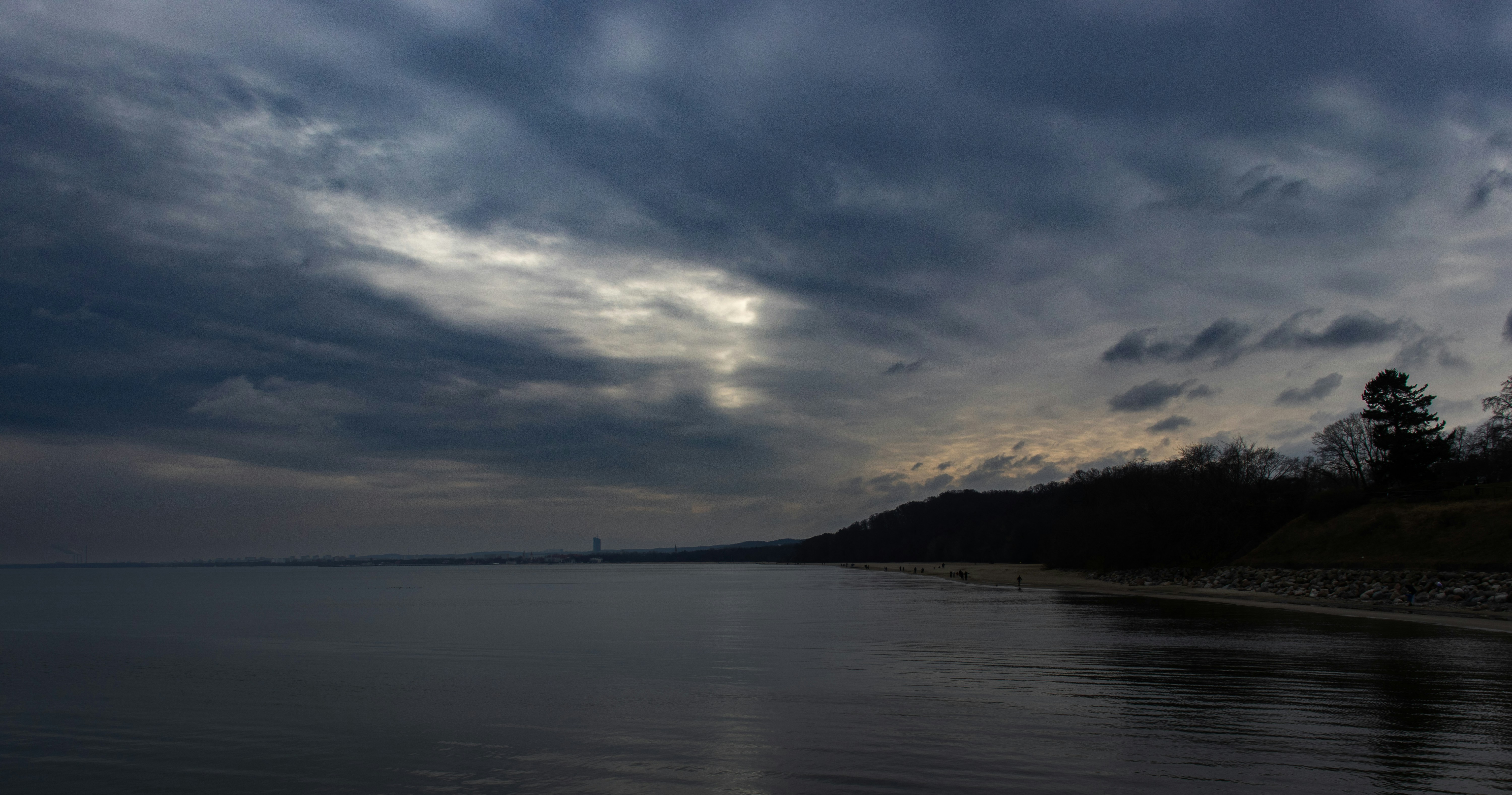 Un cielo nublado y dramático sobre un lago sereno y una costa boscosa.