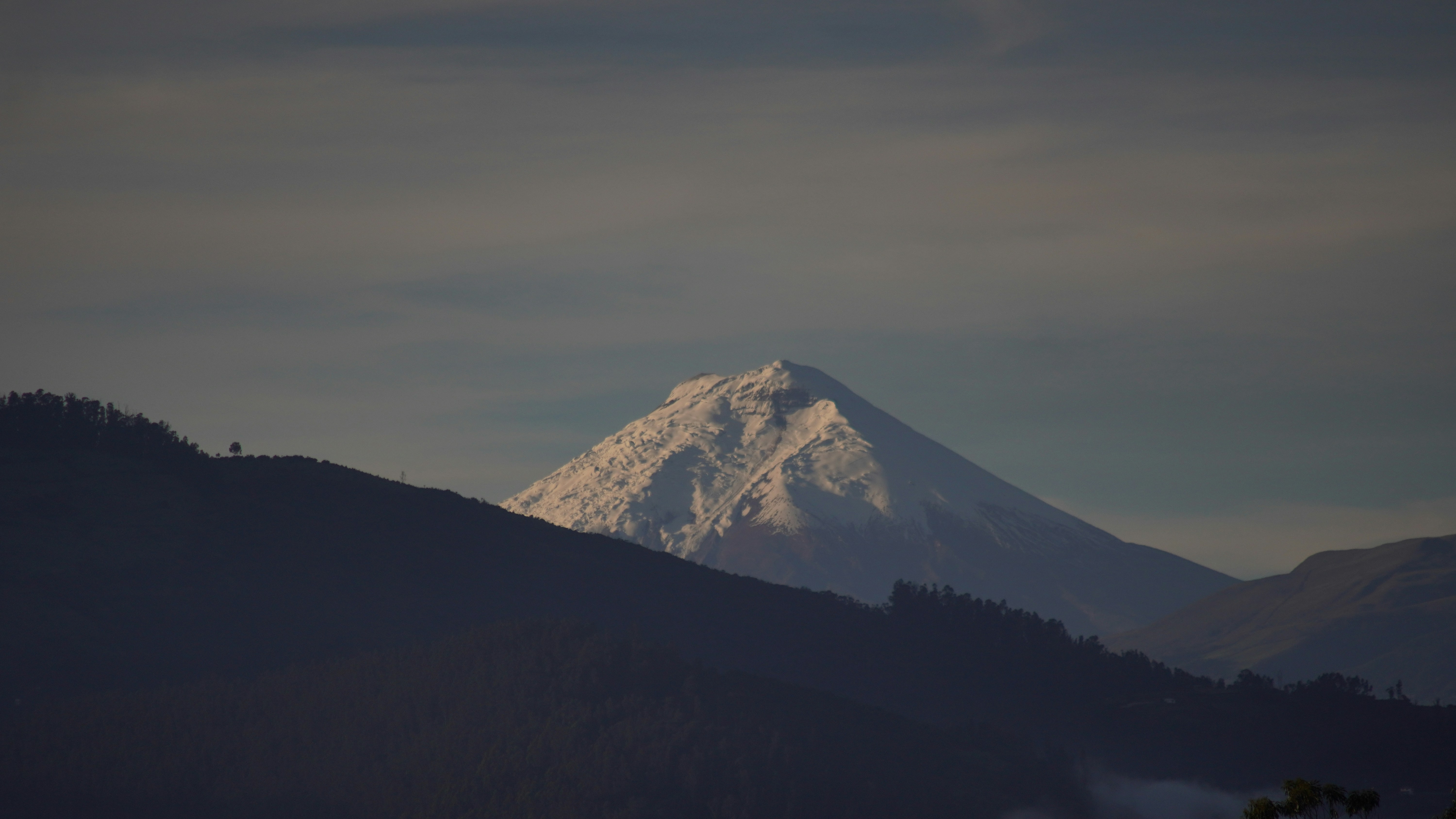 Snow-capped mountain peak rising above darker hills.