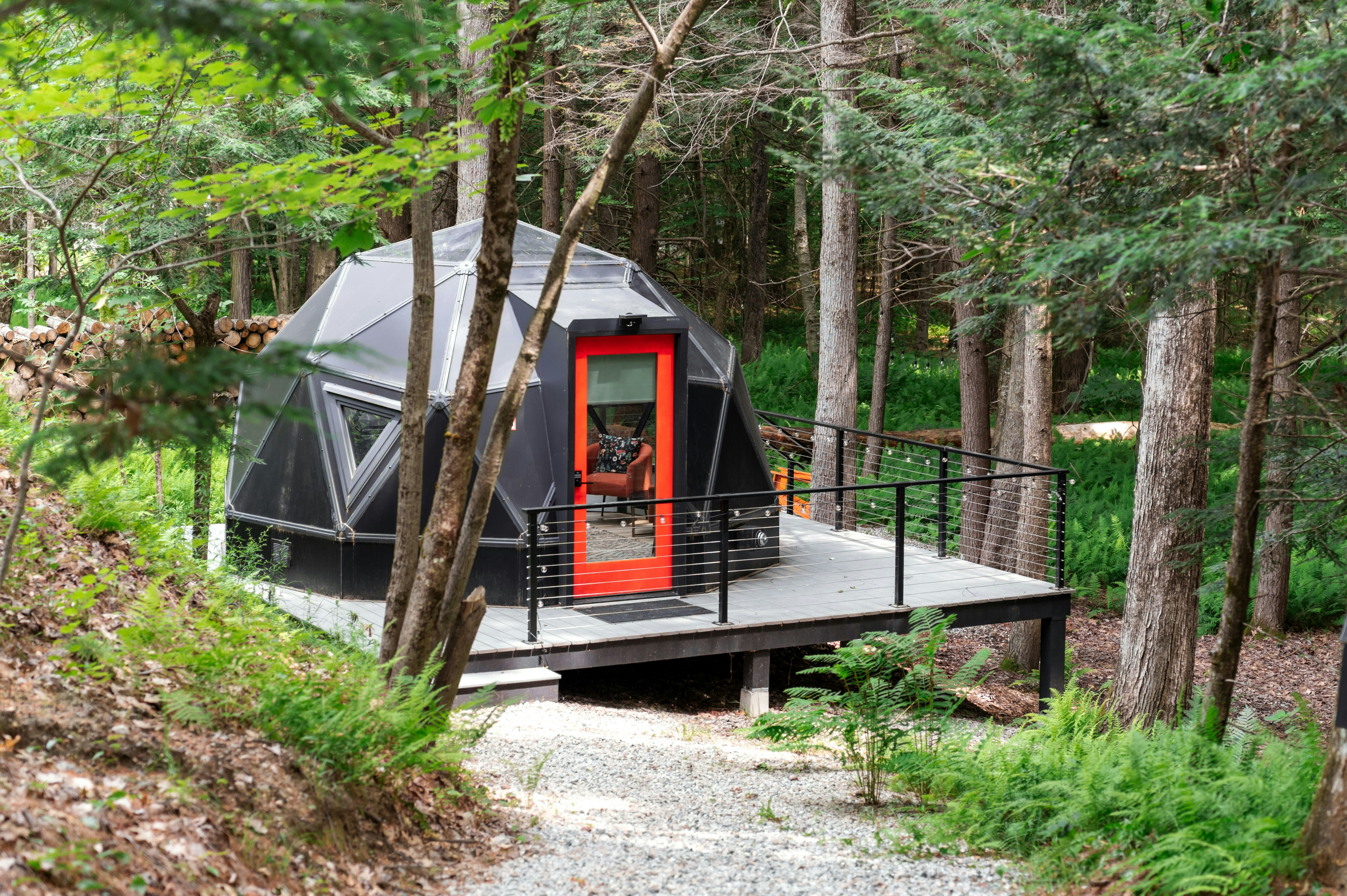Modern black geodesic dome with orange door in forest