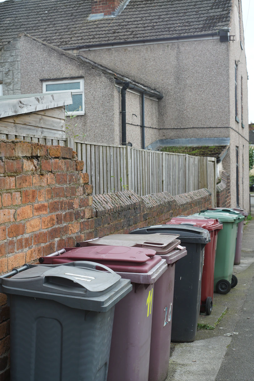 Multiple colorful wheelie bins lined up along a brick wall
