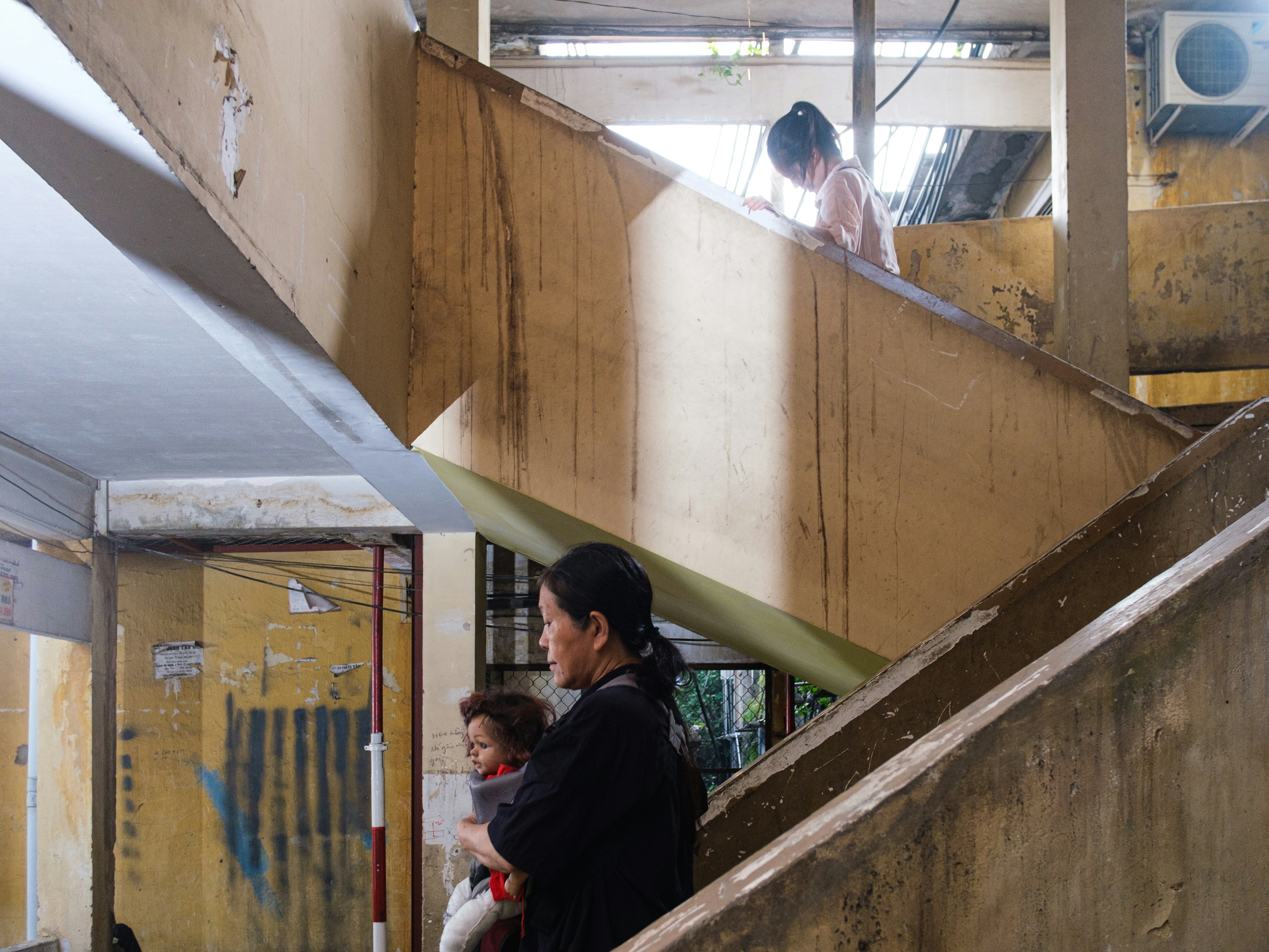 Woman holds child as another child climbs concrete stairs.