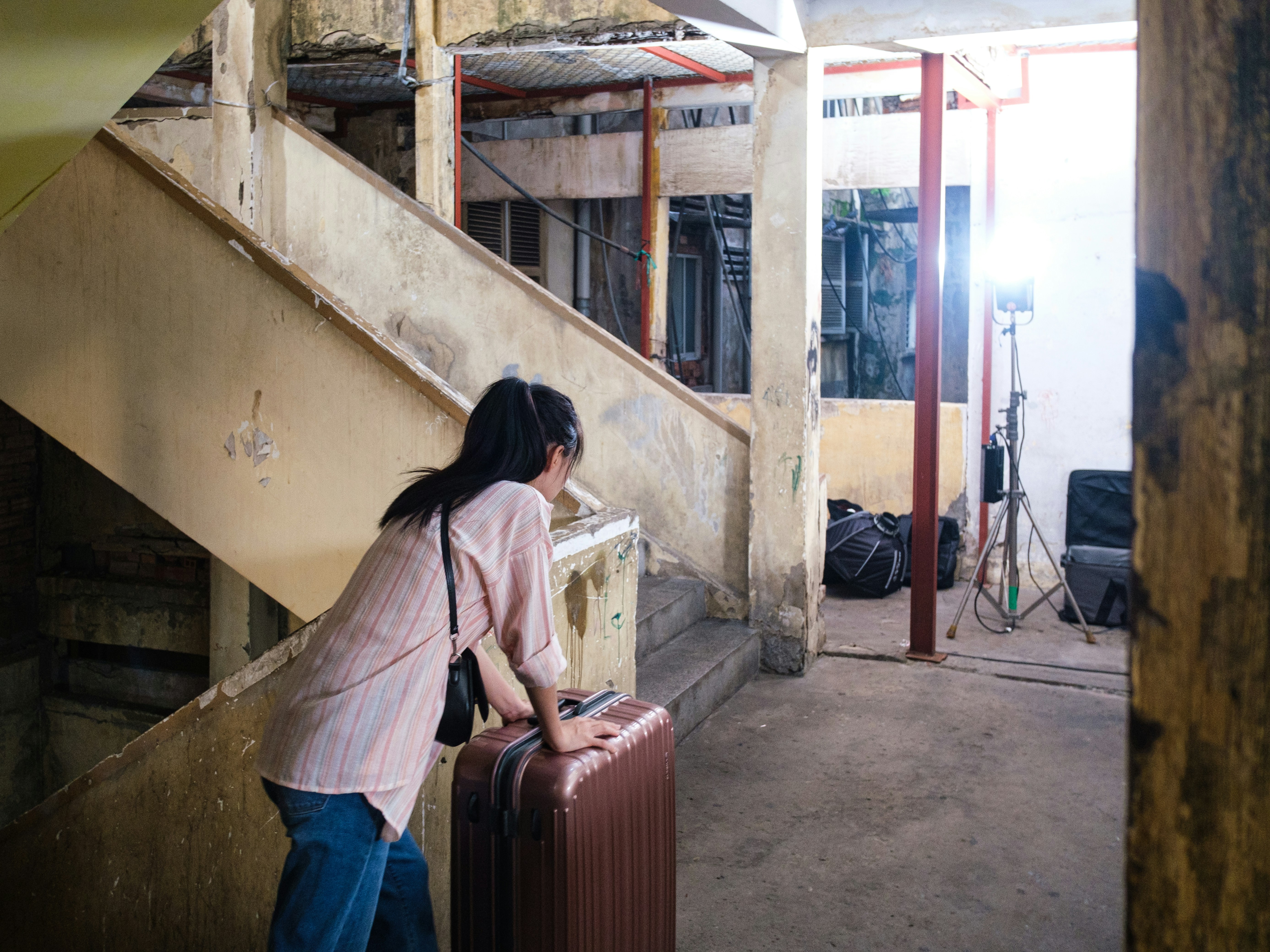 Wanita dengan koper berdiri di dekat tangga tua di gedung.