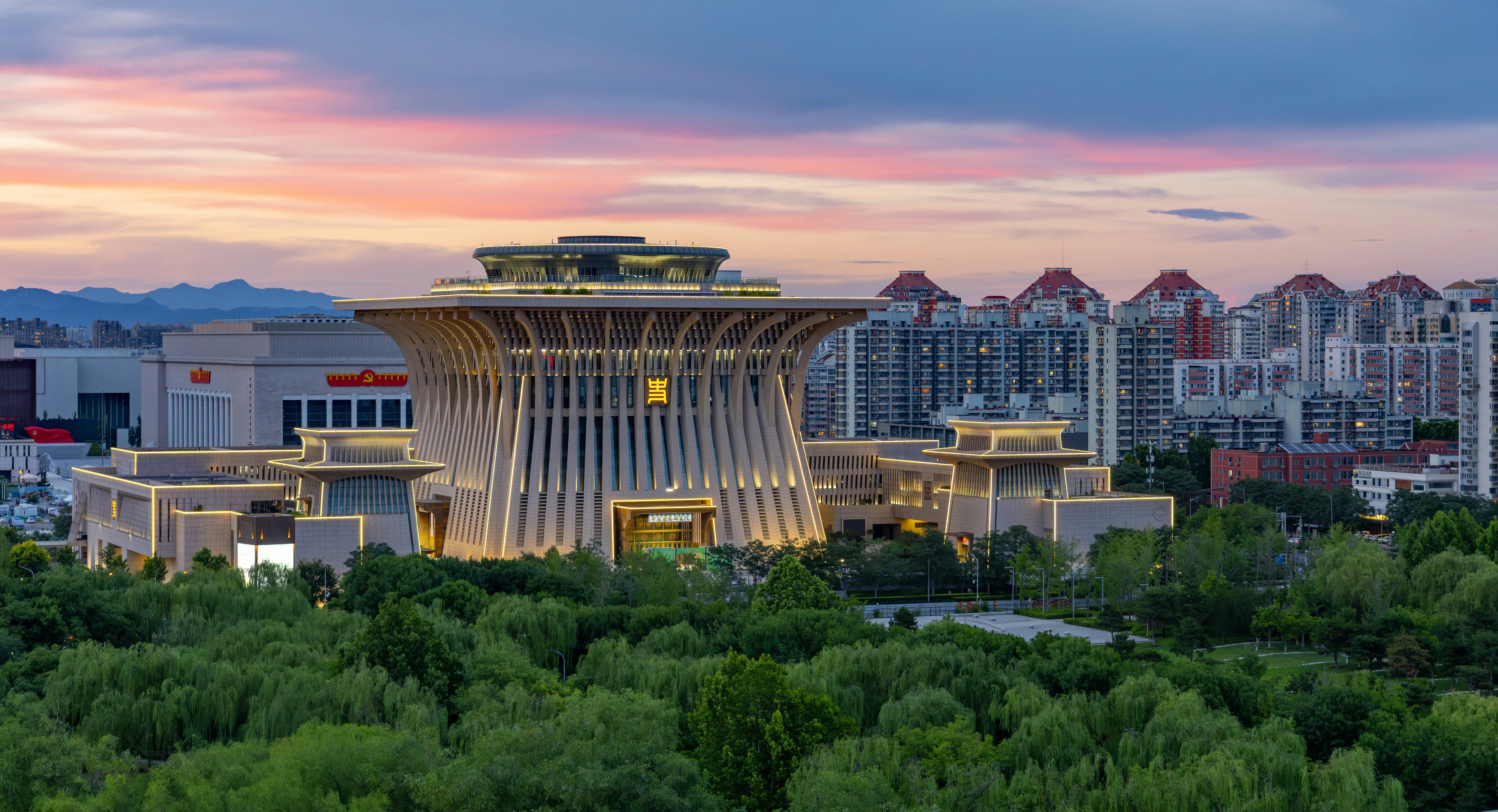 Illuminated modern building against a vibrant sunset sky and cityscape.