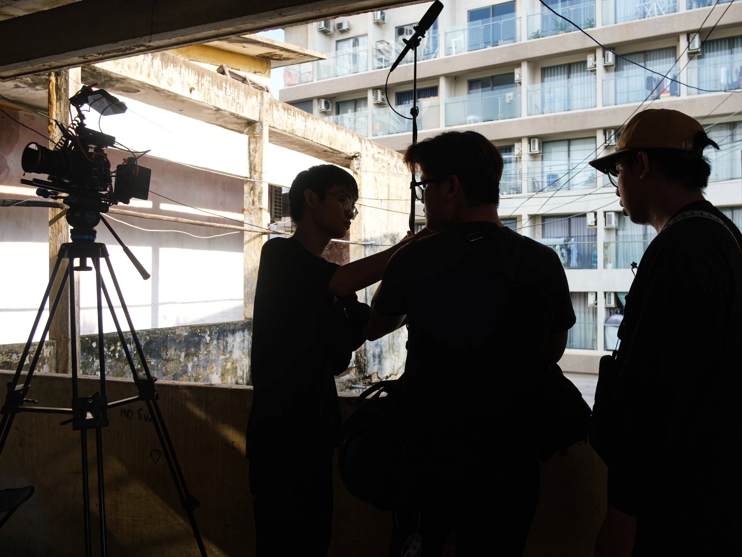 Film crew in silhouette on location, with a camera on a tripod and a boom microphone