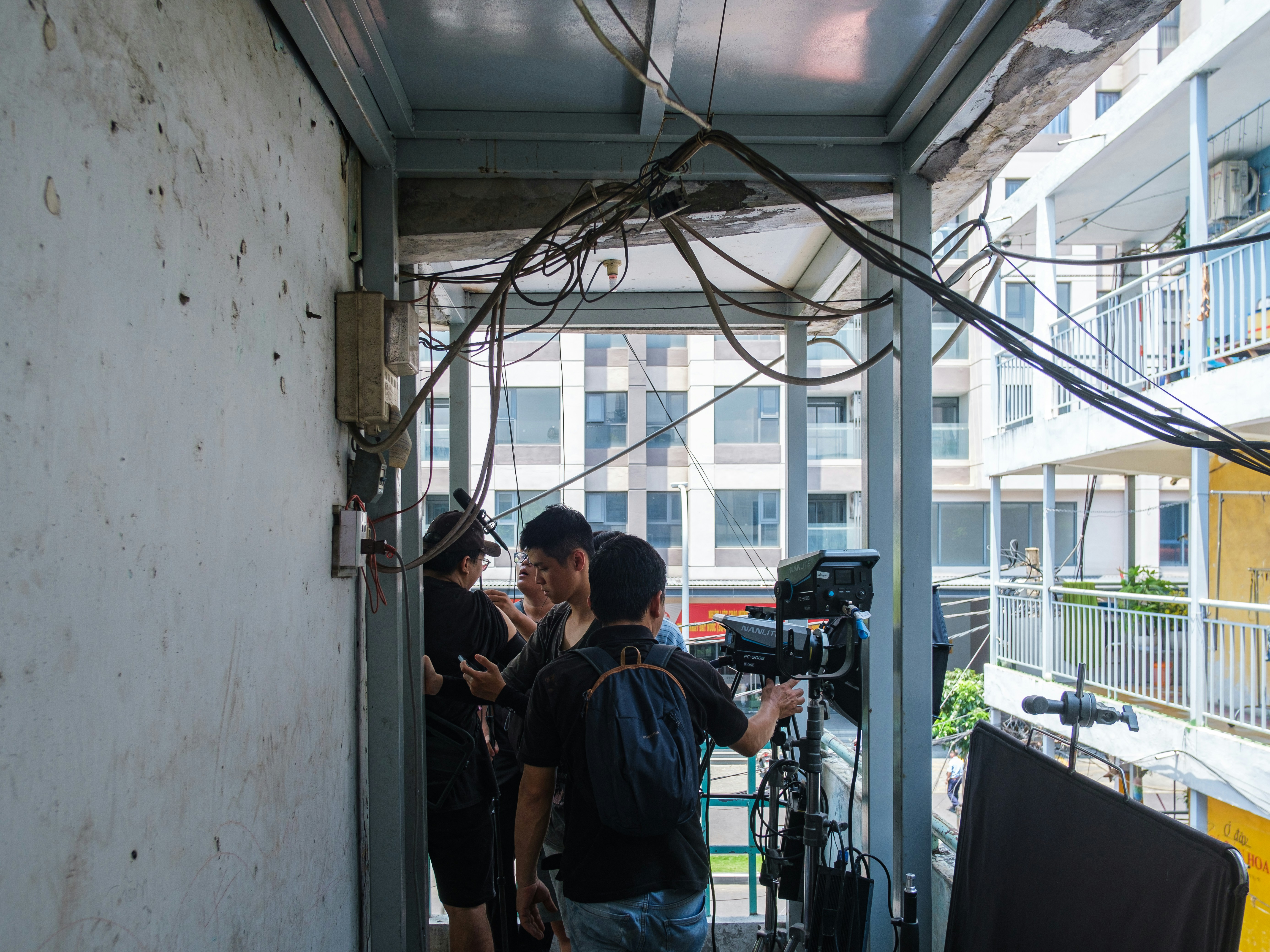 Three people with camera equipment on a narrow outdoor walkway.