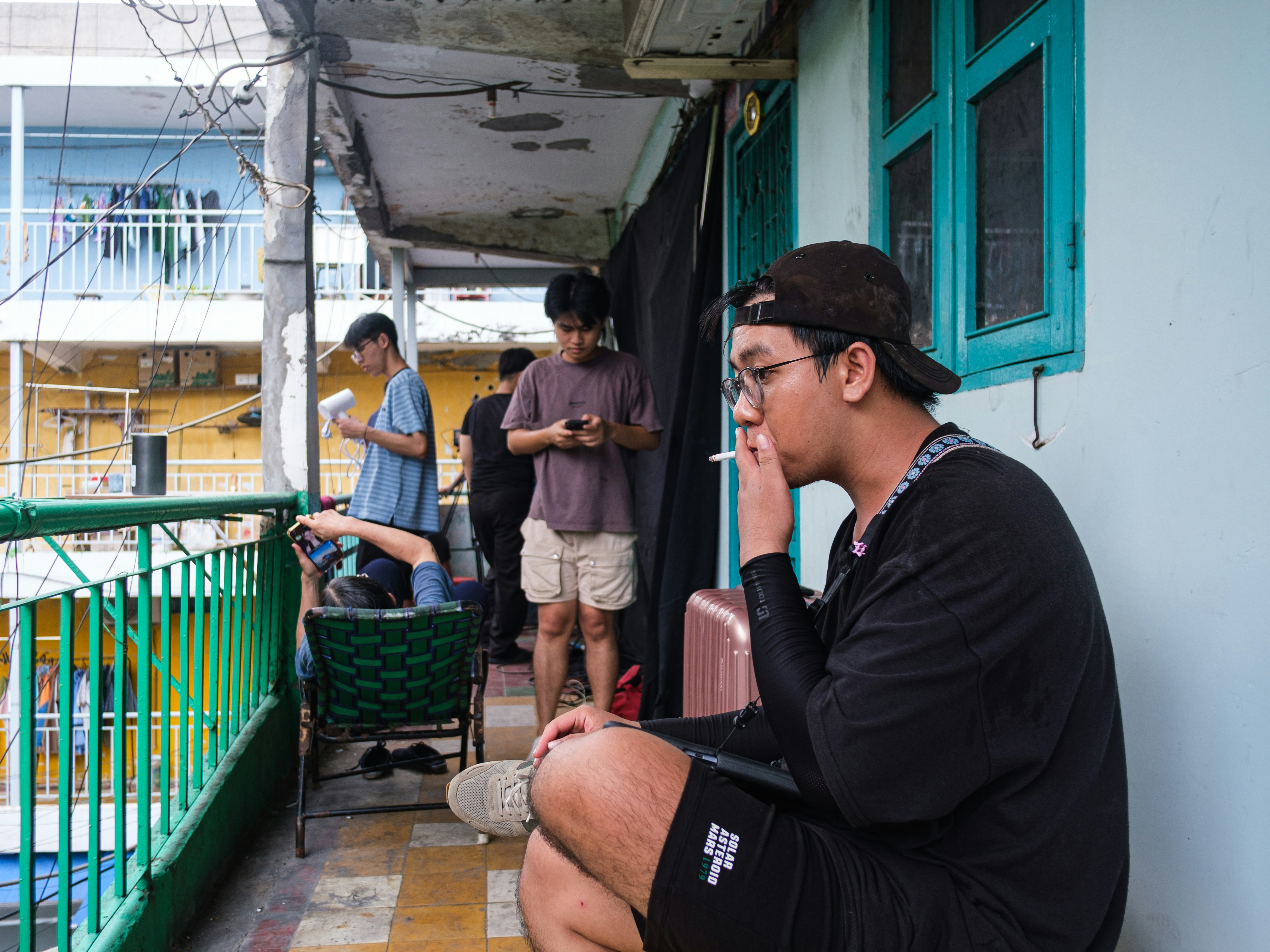 A man smokes a cigarette on a busy urban balcony.