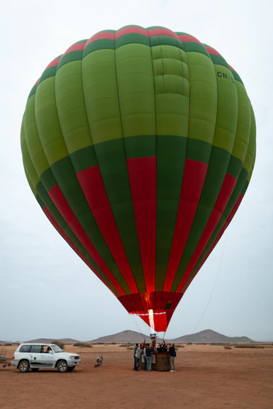 Green and red hot air balloon with people in desert