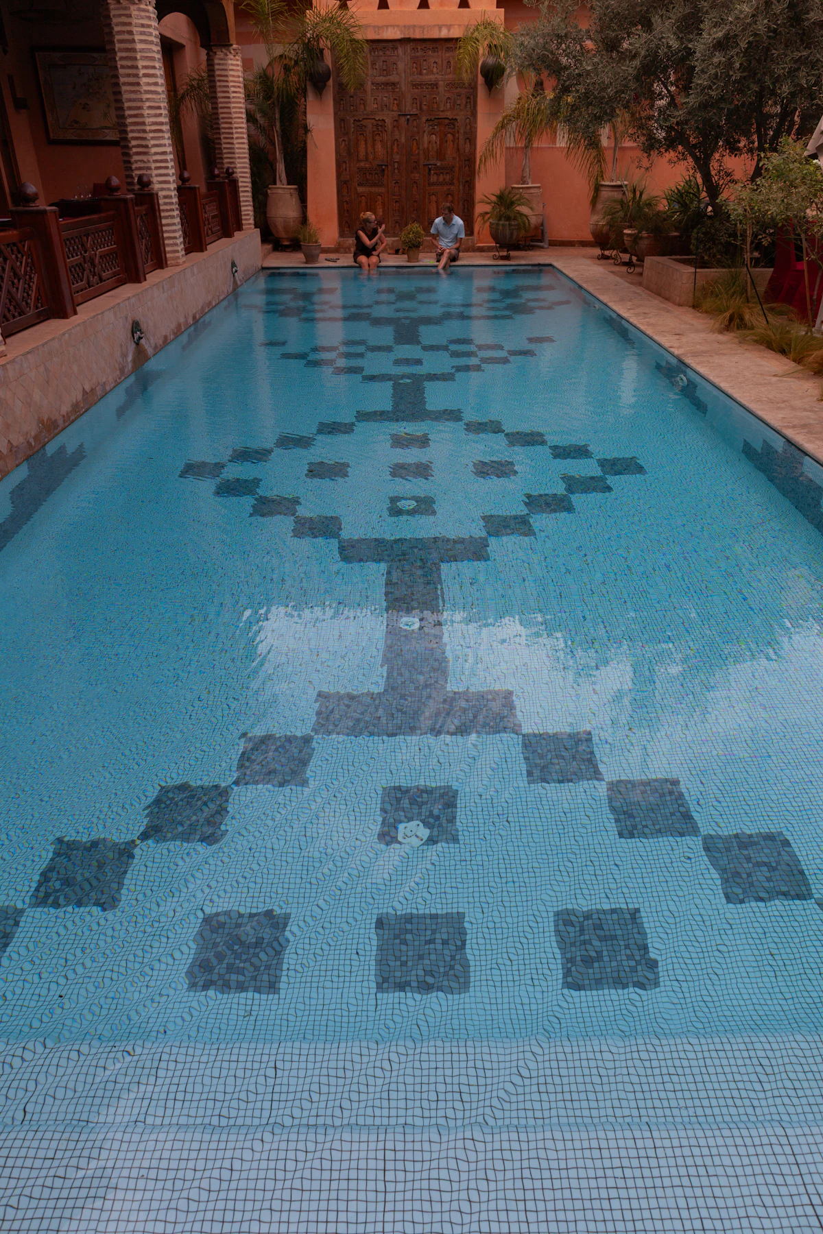 Piscine en mosaïque géométrique dans un patio marocain aux murs ocre, Marrakech