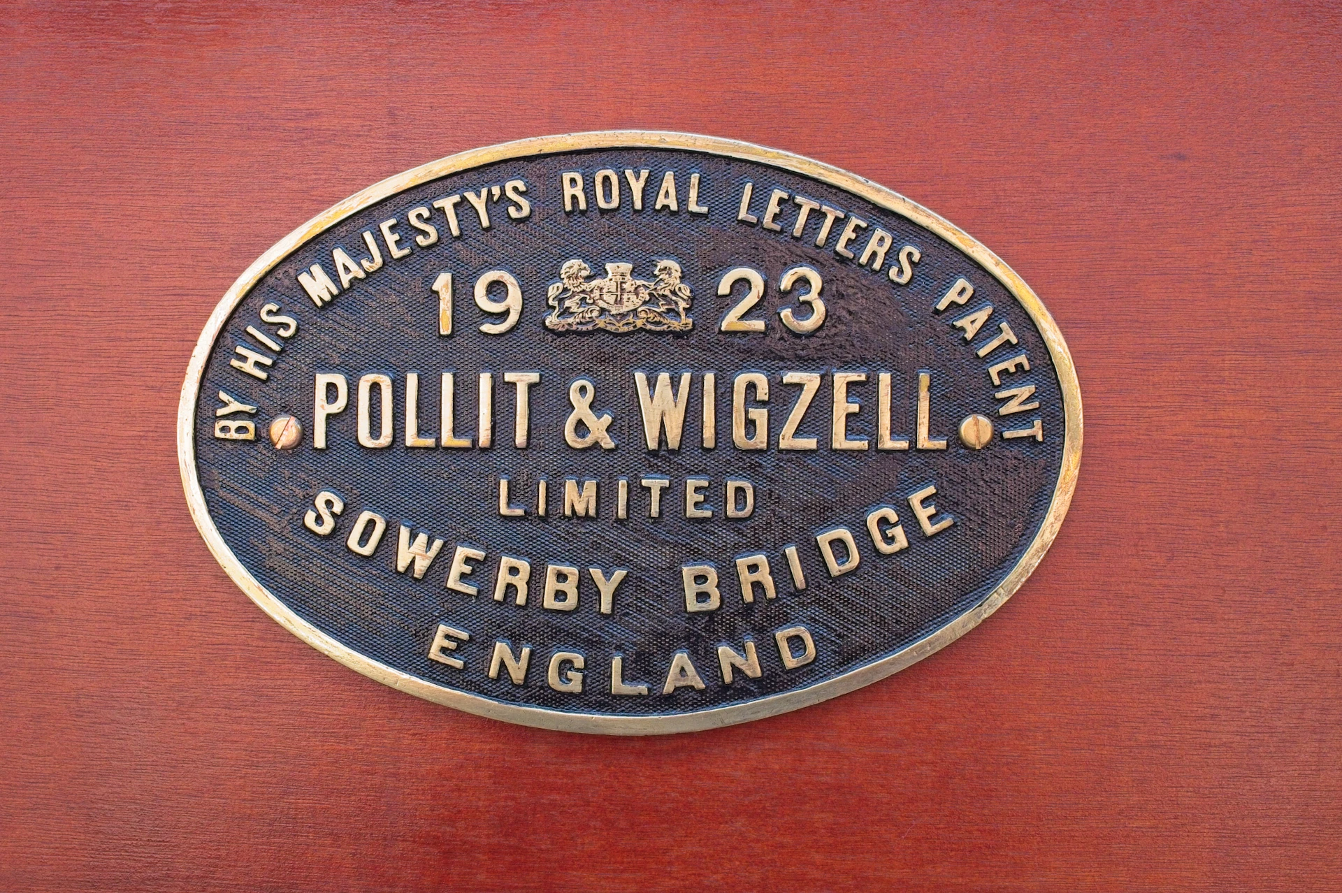 Oval brass name plate with raised lettering mounted on a red painted surface