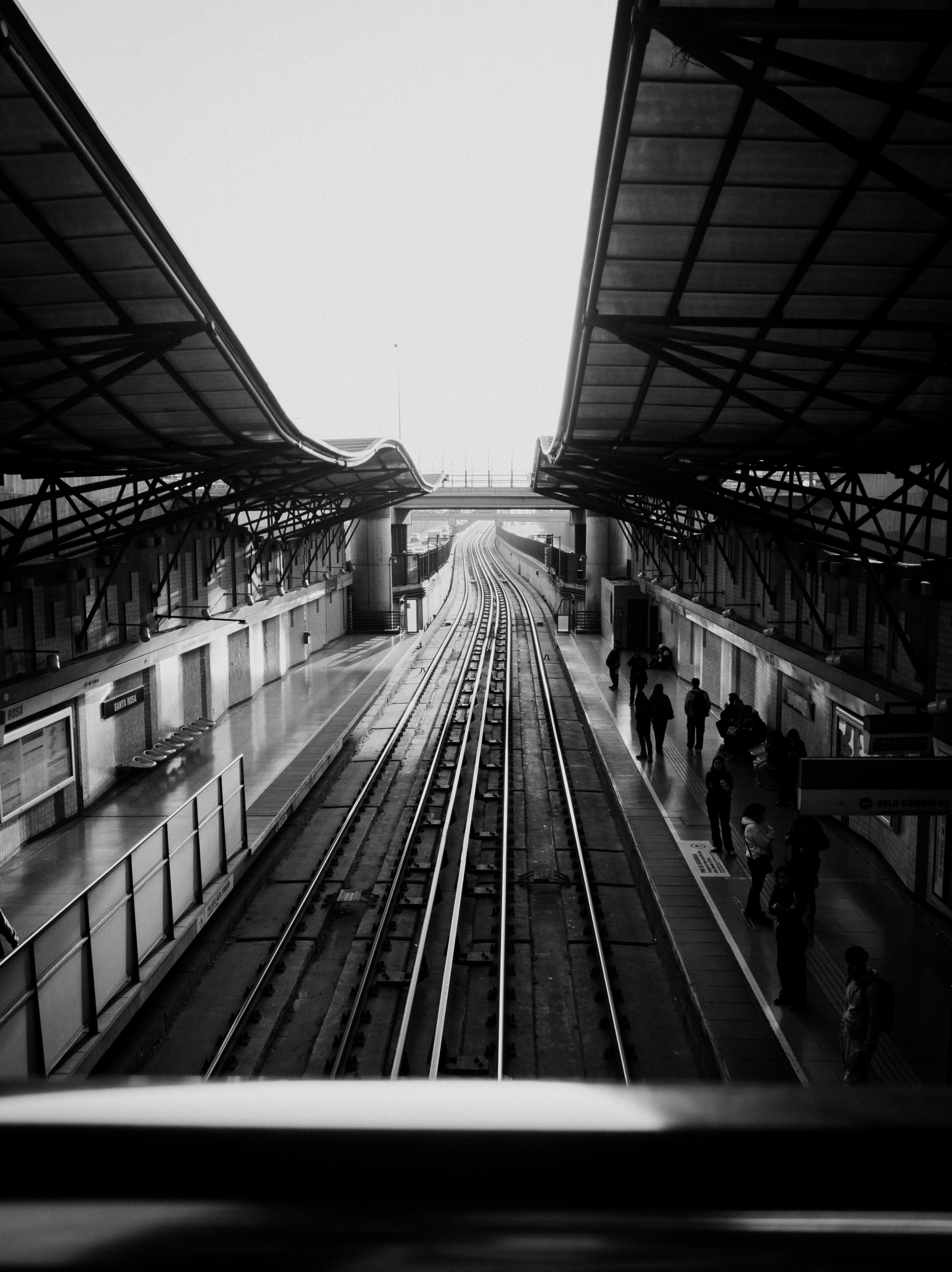 Elevated train station in black and white with passengers.