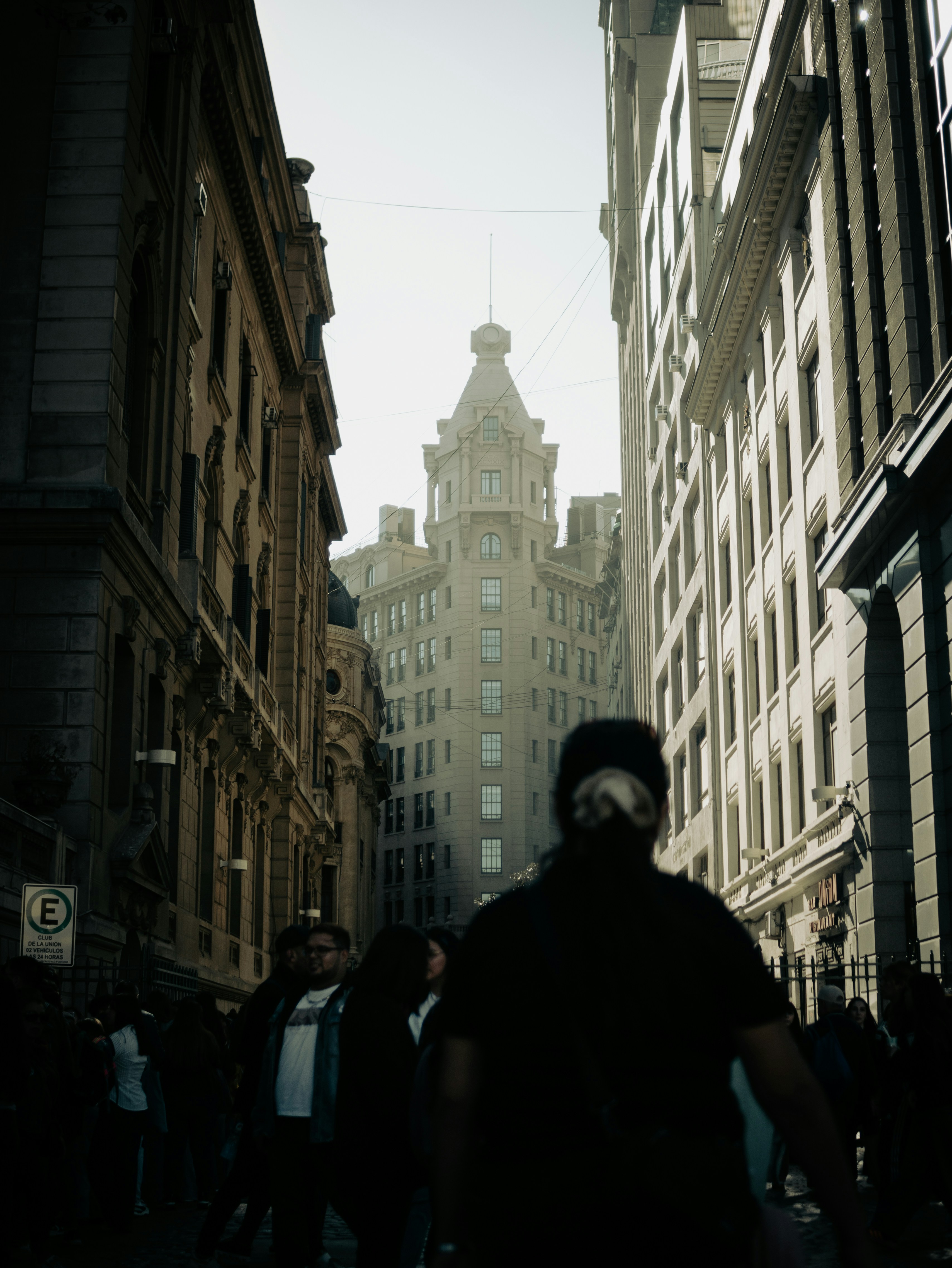 Masked person walks city street towards grand building.