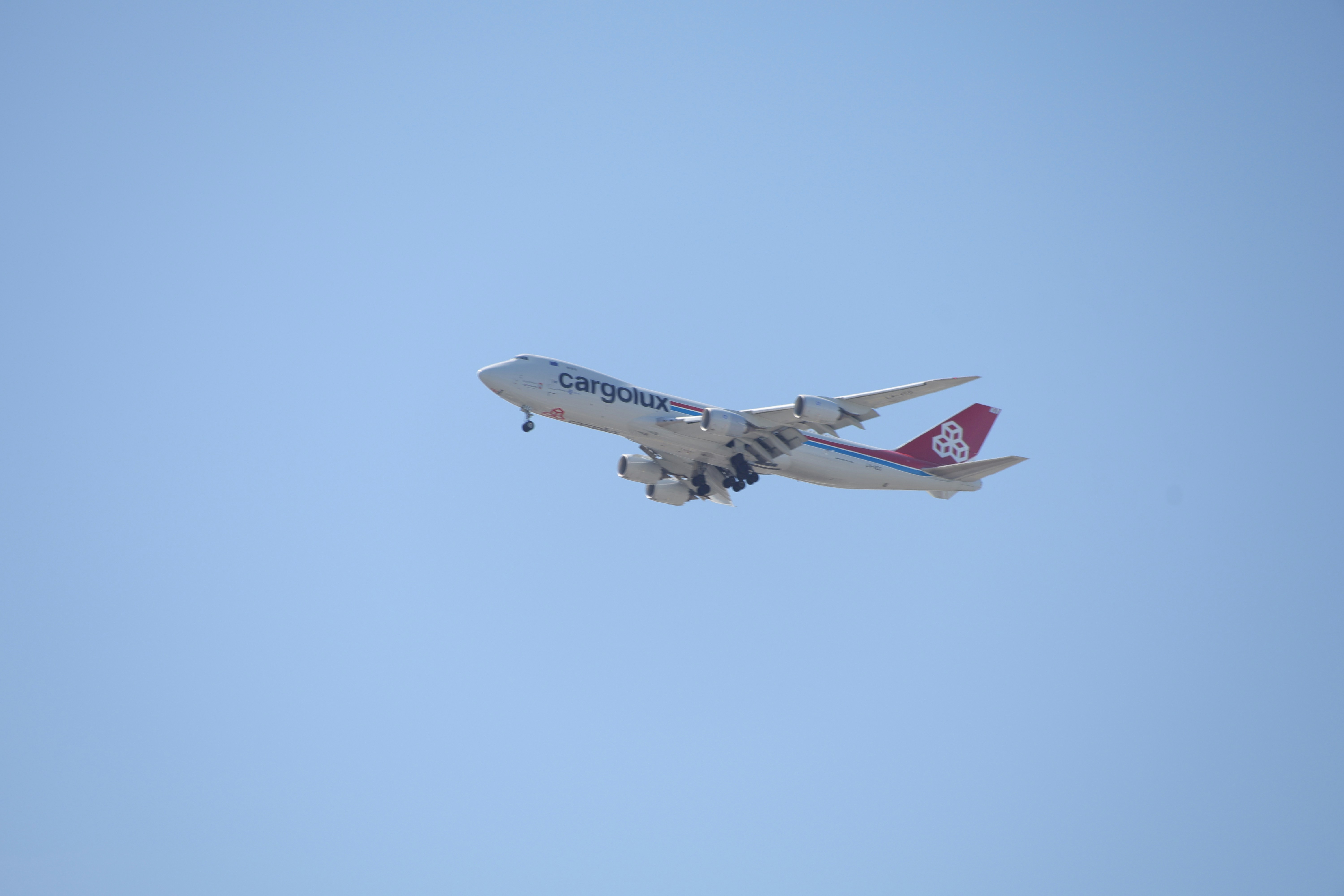 White and red airplane flying with landing gear down.