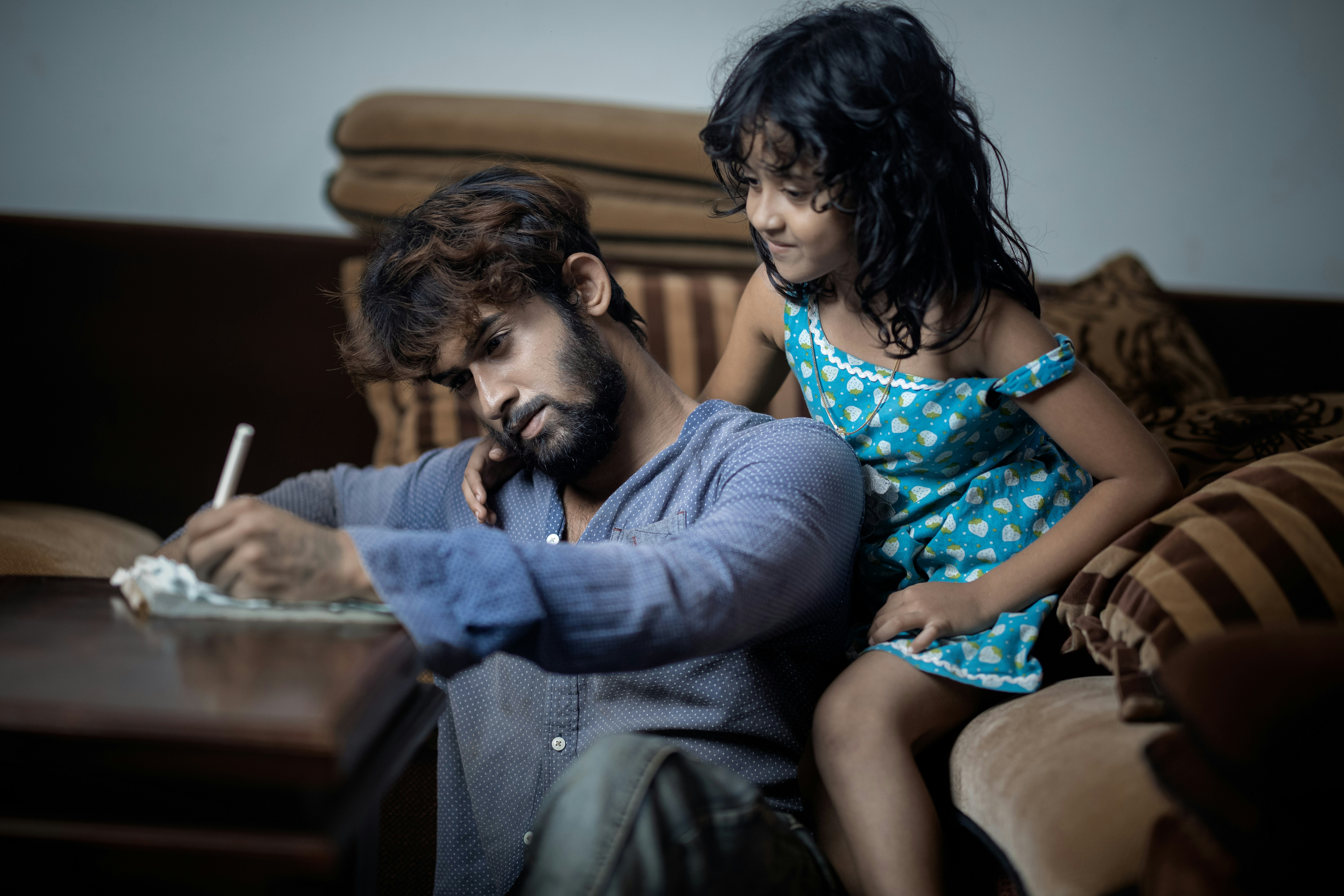 A father writing while his daughter watches him intently, illustrating financial education.