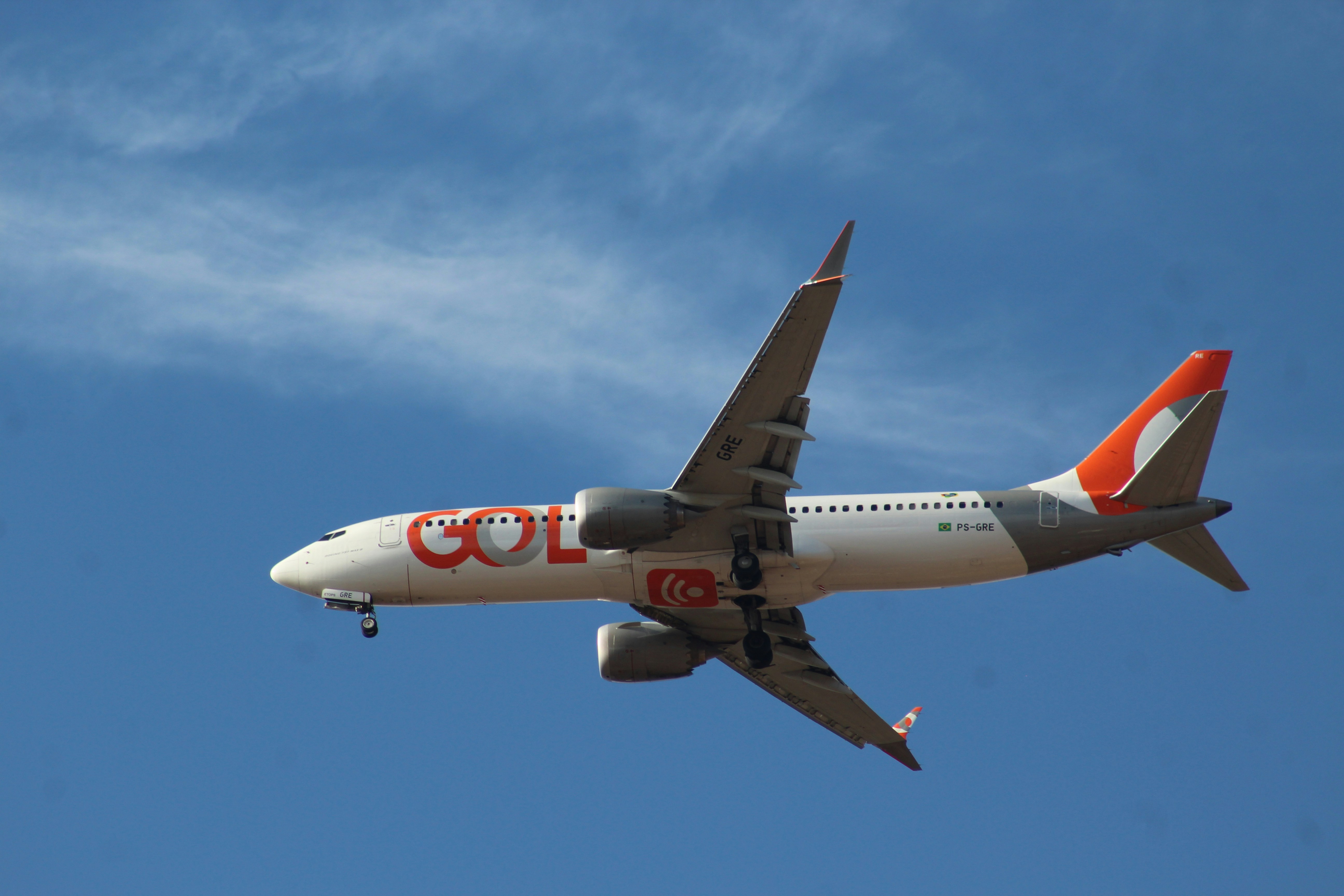 Gol passenger airplane with landing gear down against blue sky.