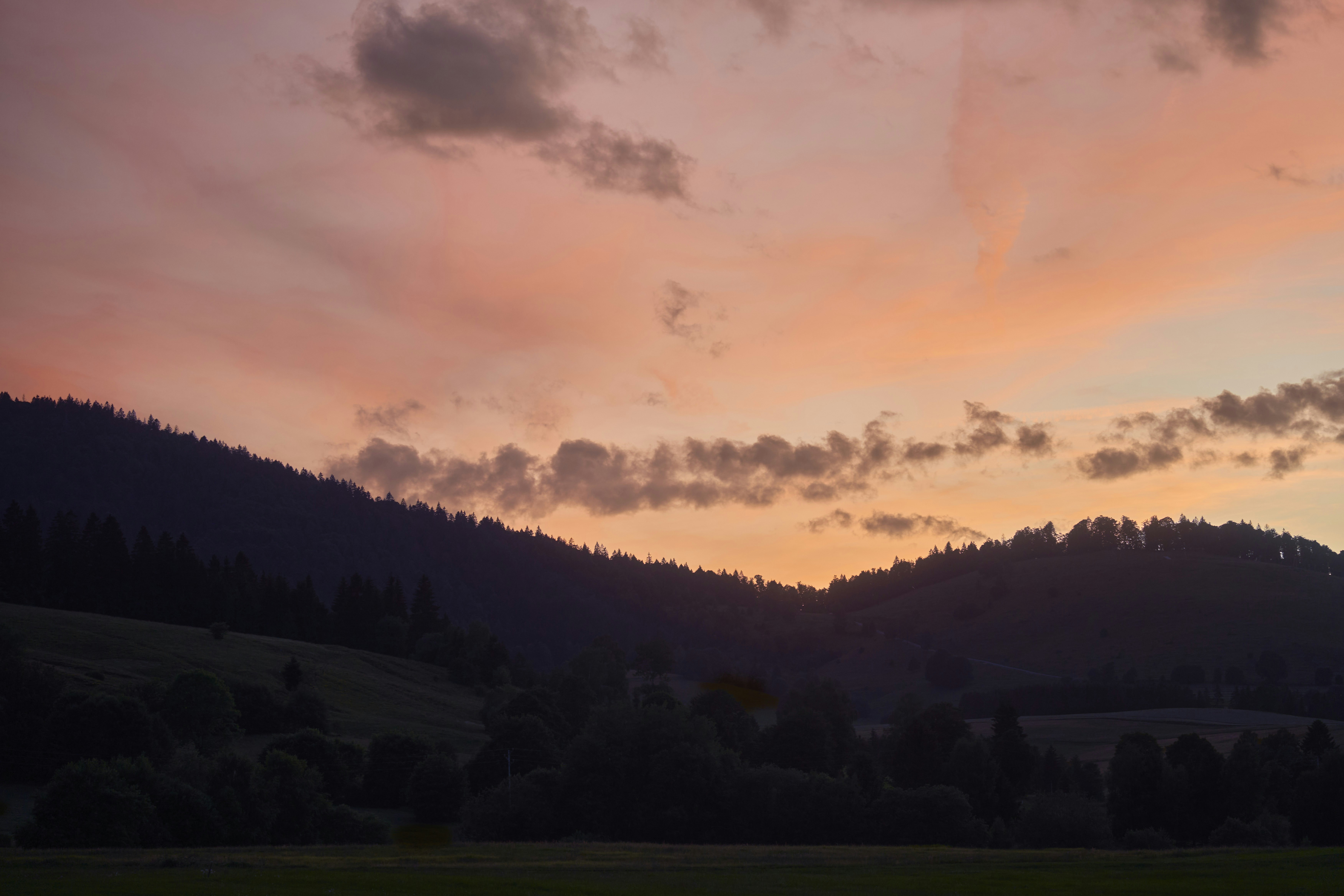 A vibrant sunset sky over dark, forested hills.