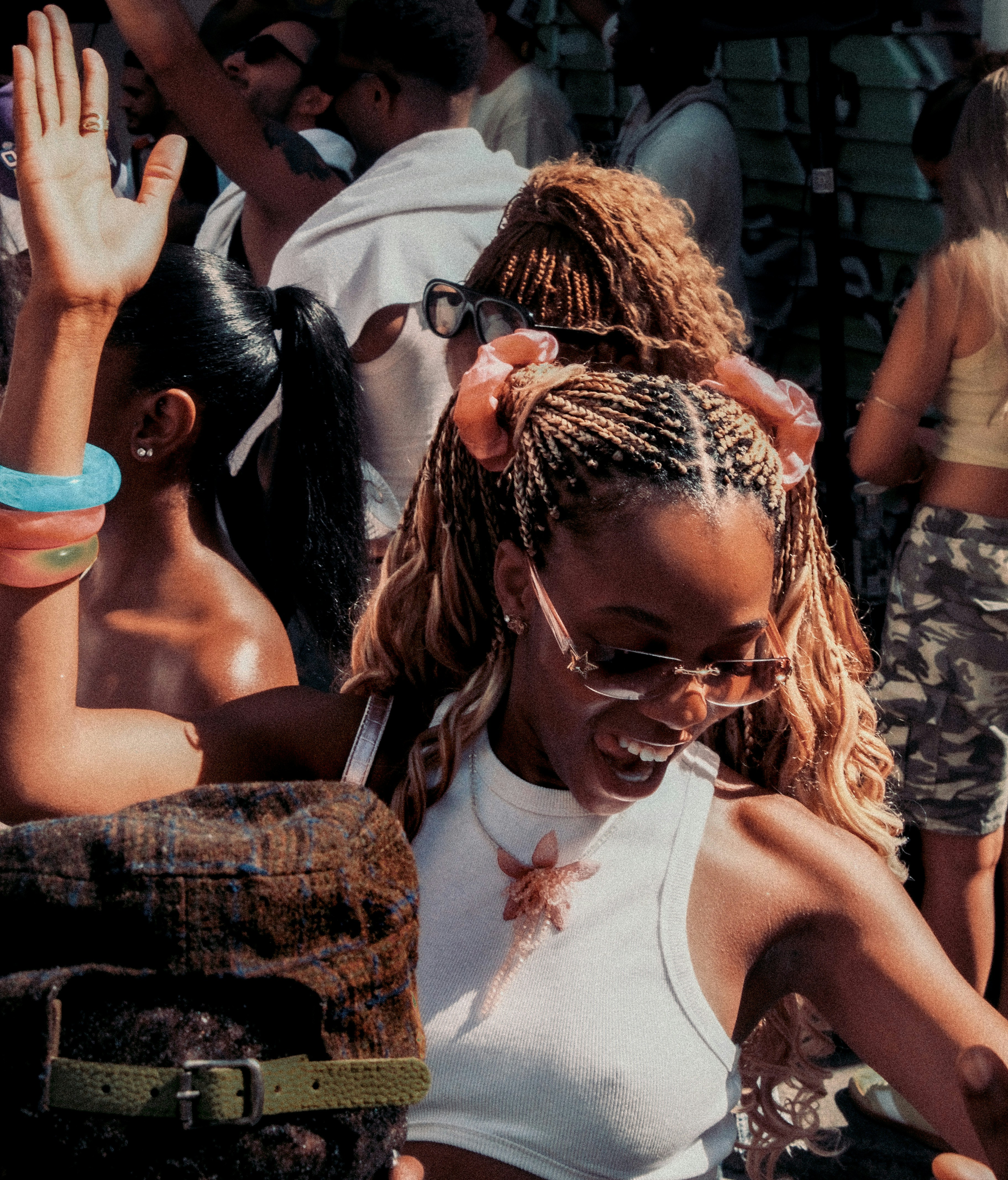 Cheerful woman with braided hair and sunglasses dancing outdoors.