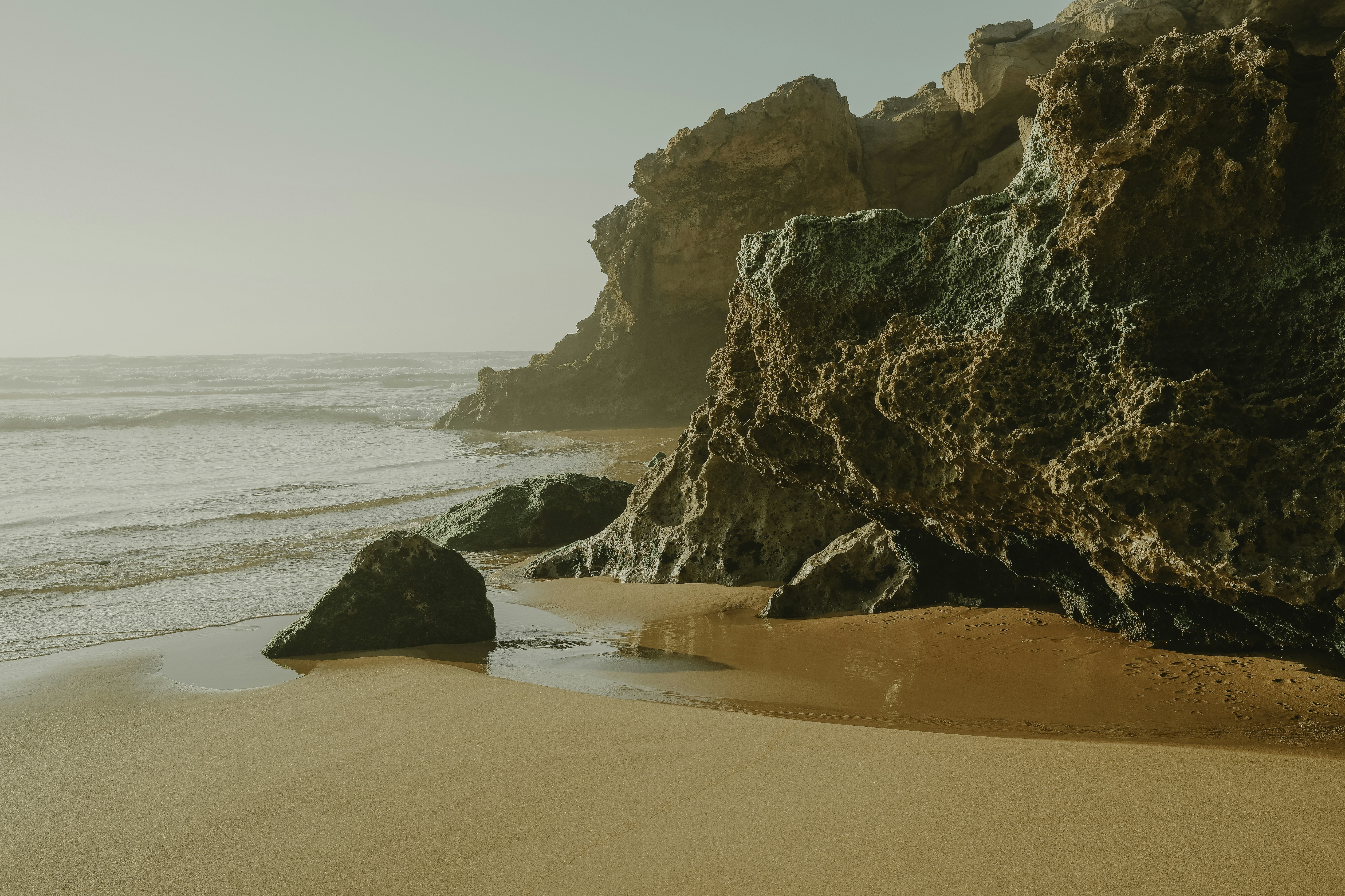 Sunlit sandy beach with large rocky cliffs and ocean waves