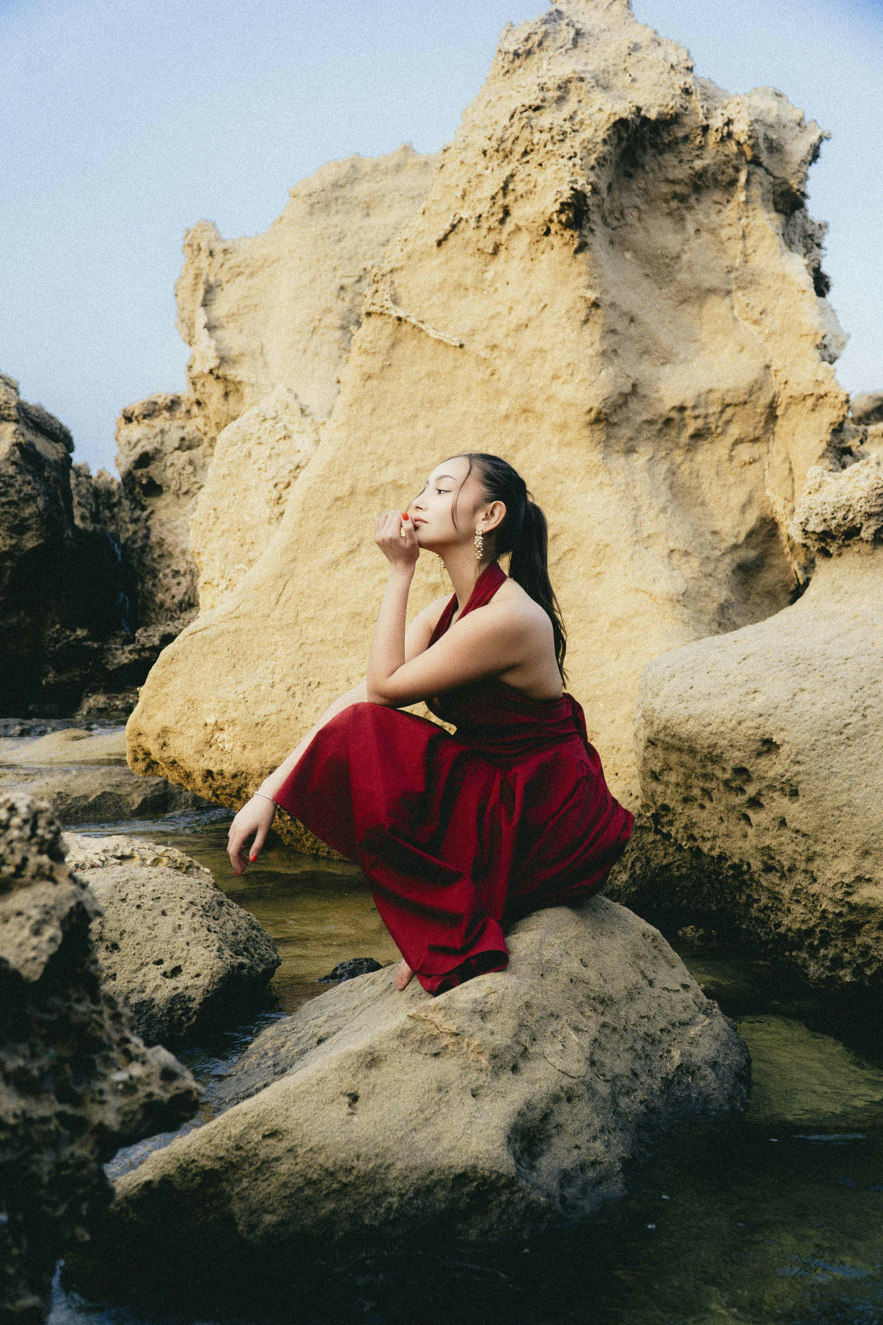 Serene woman in red dress on rocky shore