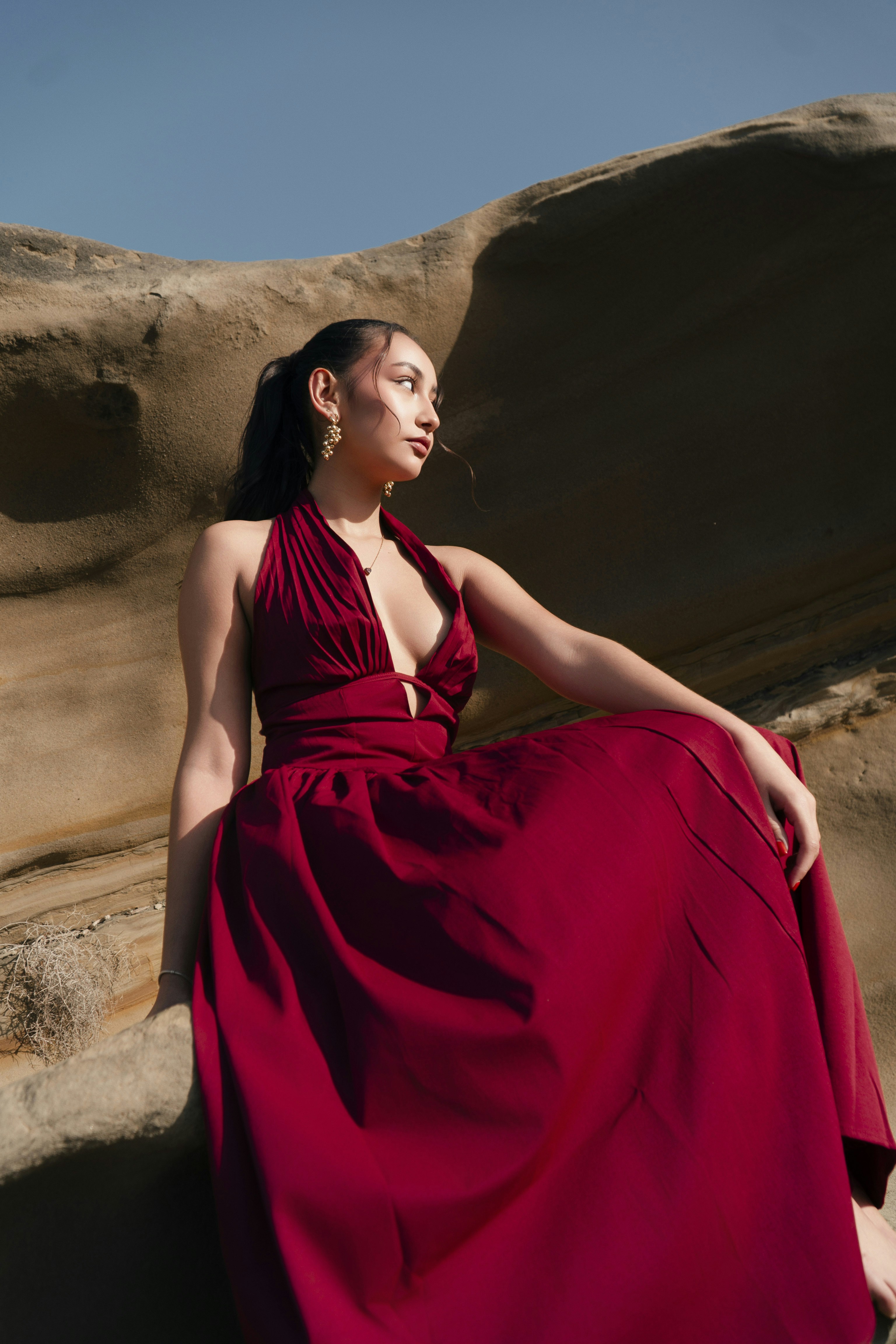 Woman in red halter dress sitting on sunlit rocks